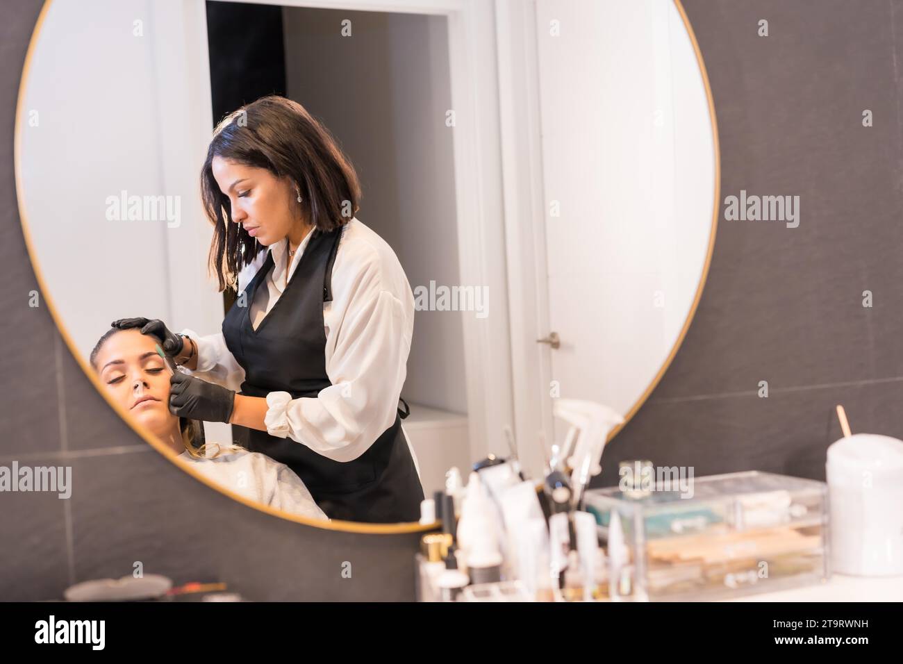 Ein Bild auf einem Spiegel eines Friseurs, der die Augenbrauen einer Frau stylt, die auf einem Stuhl in einem Schönheitssalon sitzt Stockfoto