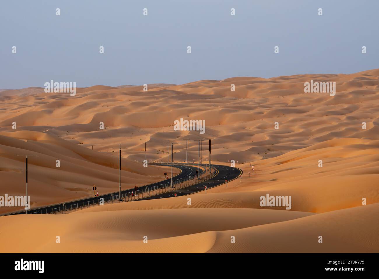 Eine gewundene Wüstenstraße in der Wüste Rub Al Khali in der Nähe von Liwa, VAE, mit riesigen Sanddünen um sie herum. Stockfoto