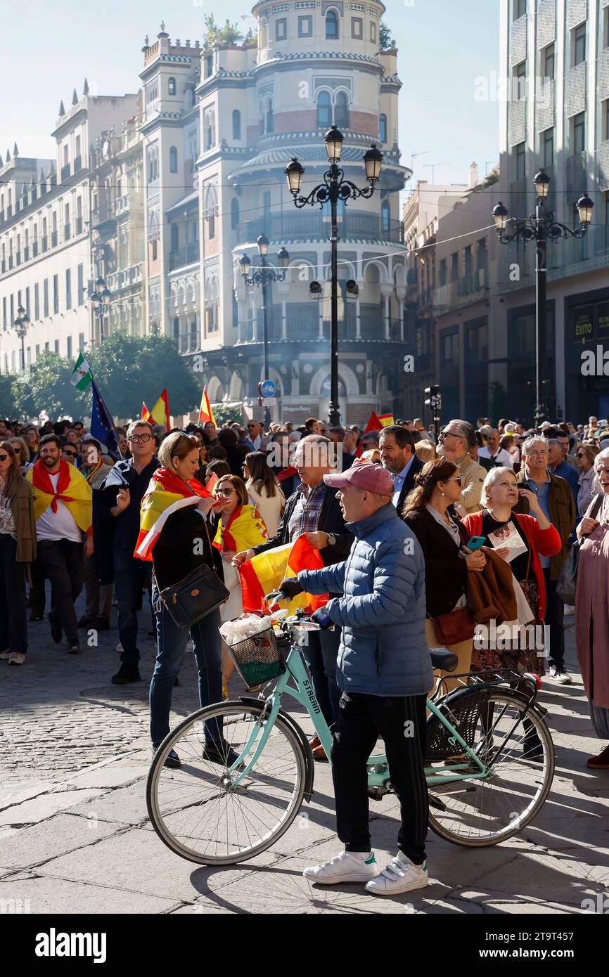 Ein Mann, der sein Fahrrad an einer großen Gruppe von Menschen vorbeischiebt, bei einer politischen Kundgebung in Sevilla, Andalusien, Spanien Stockfoto