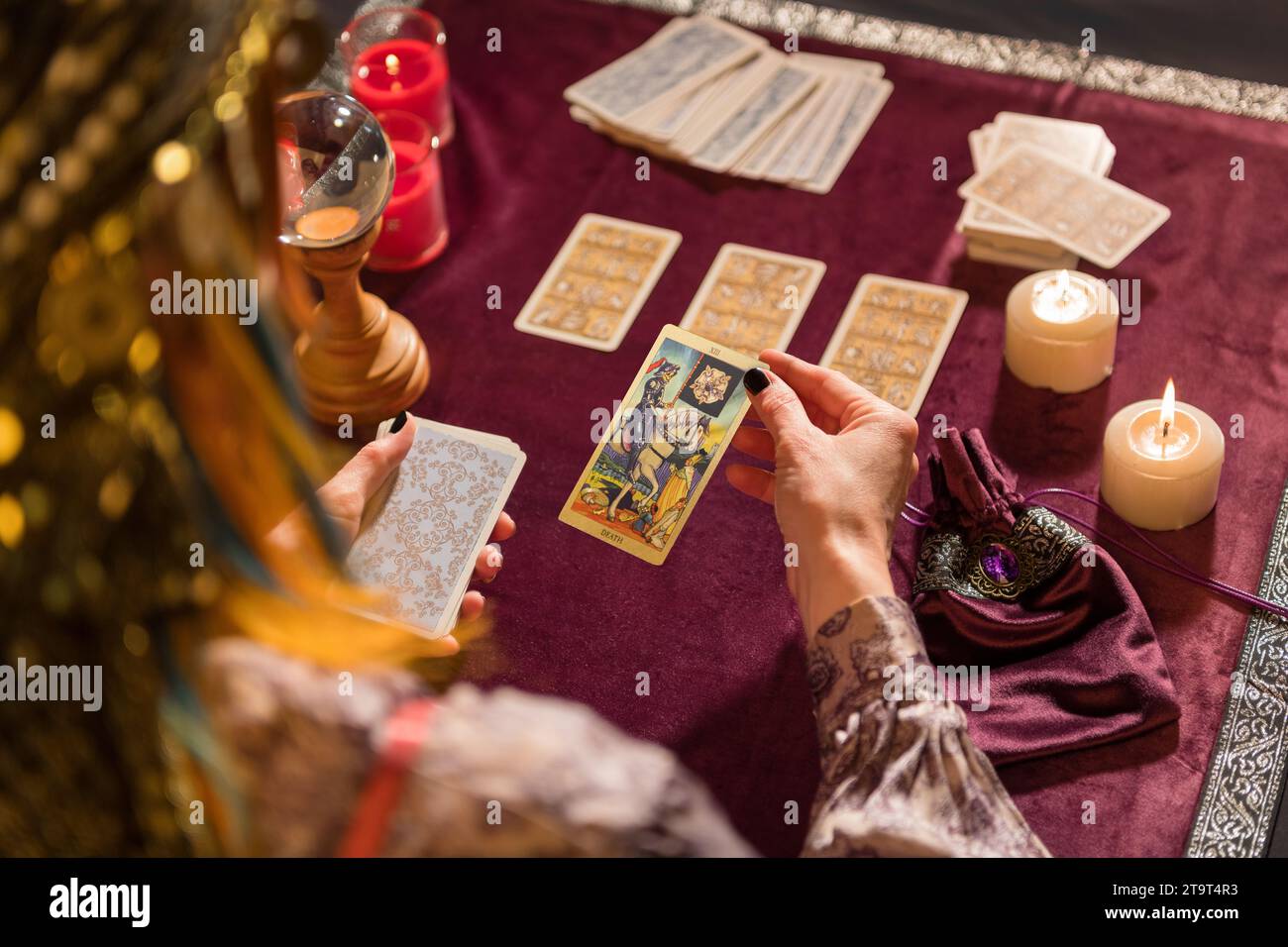 Rückansicht der Ernte nicht erkennbare weibliche Wahrsagerin im Kostüm, die Tod-Tarot-Karte auswählt, während sie mit brennenden Kerzen und Kristall am Tisch sitzt Stockfoto