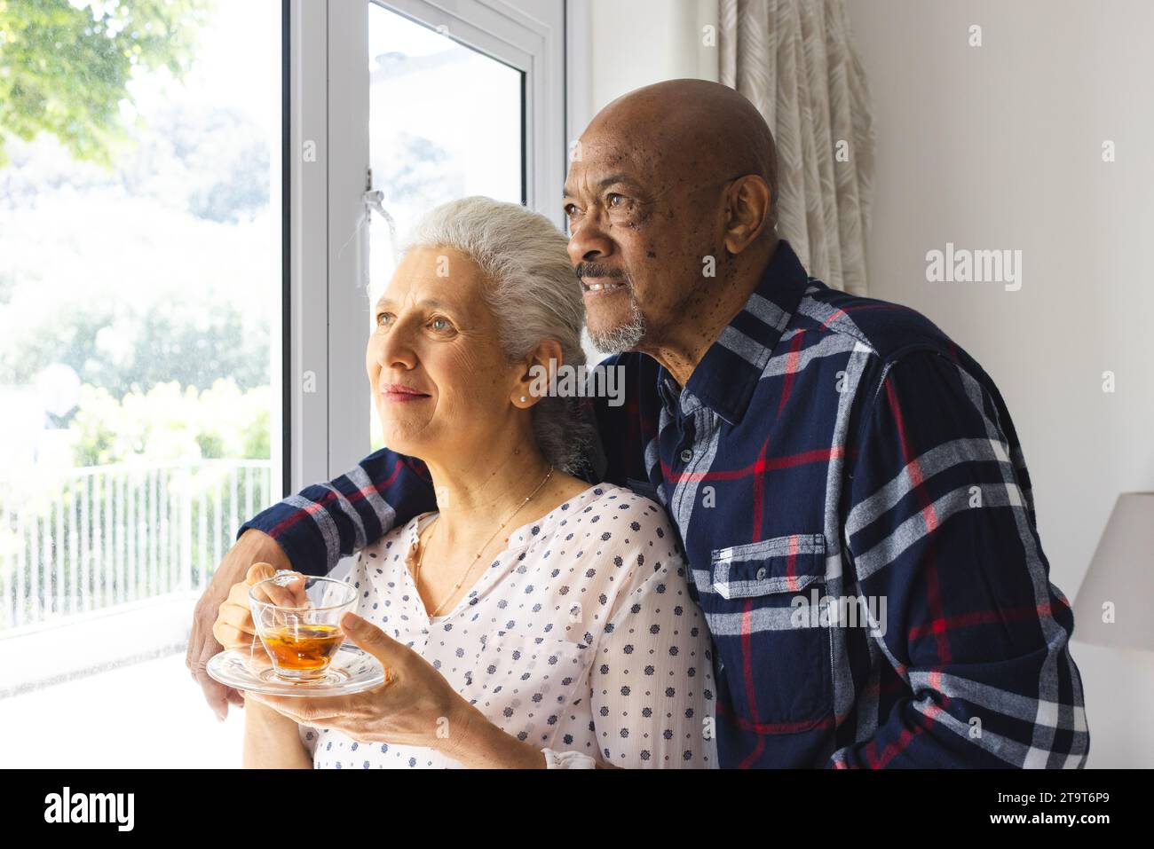 Diverse Seniorenpaare trinken Tee, umarmen und aus dem Fenster auf das sonnige Haus schauen. Lebensstil, Ruhestand, Seniorenleben, Zweisamkeit und Haushalt Stockfoto