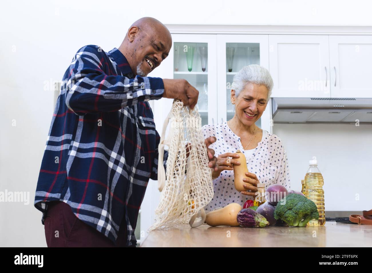 Glückliches, vielseitiges Seniorenpaar, das Lebensmittel in der Küche auspackt. Lebensstil, Ruhestand, Seniorenleben, Einkaufen, Zweisamkeit und häusliches Leben, unveränderlich Stockfoto