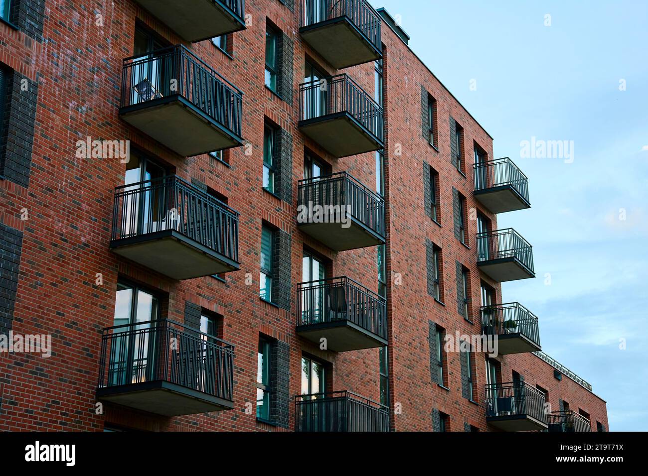 Wohnhausfassade mit Balkonen und Fenstern. Moderne Stadtarchitektur. Appartementgebäude aus roten Ziegeln Stockfoto