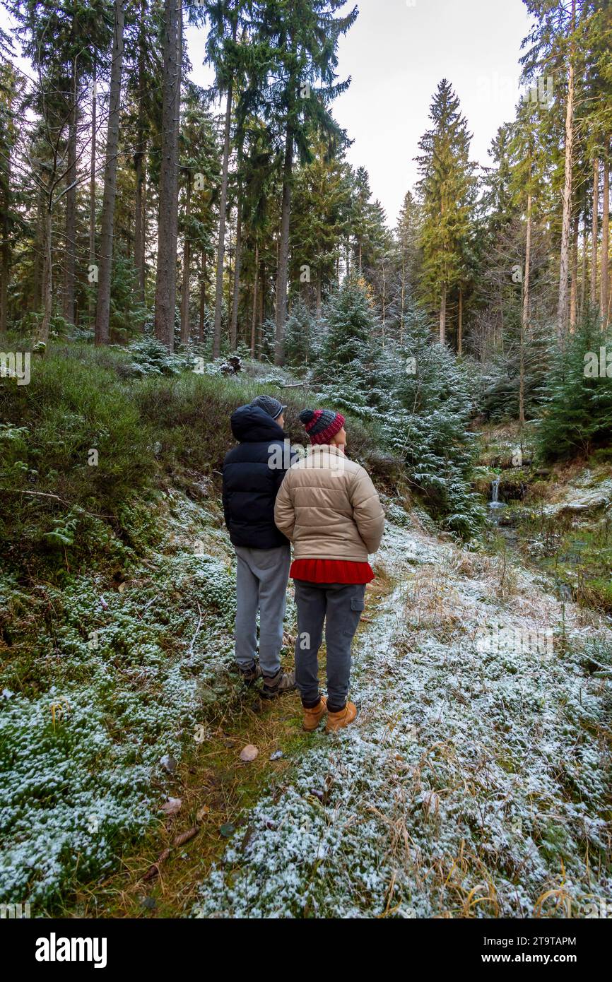 Frau mit einem kleinen Sohn mit Wackelhüten, die im herbstlichen Wald zur Linse zurückstehen Stockfoto