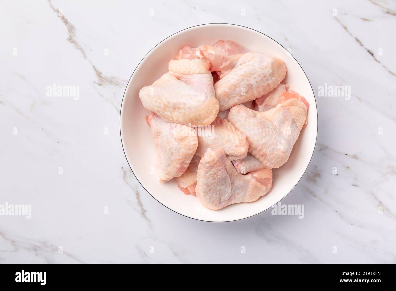 Rohe Hähnchenflügel in weißer Schüssel, zum Kochen auf Marmorhintergrund vorbereitet Stockfoto