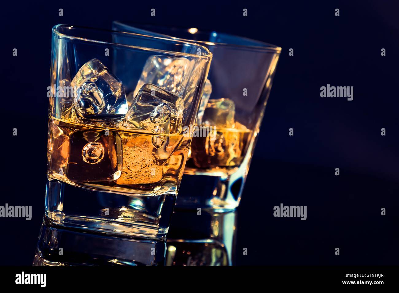 Zwei Gläser Whiskey mit Eiswürfeln auf schwarzem Hintergrund mit hellblauem Hintergrund und Reflexion, Zeit der Entspannung mit Whisky Stockfoto