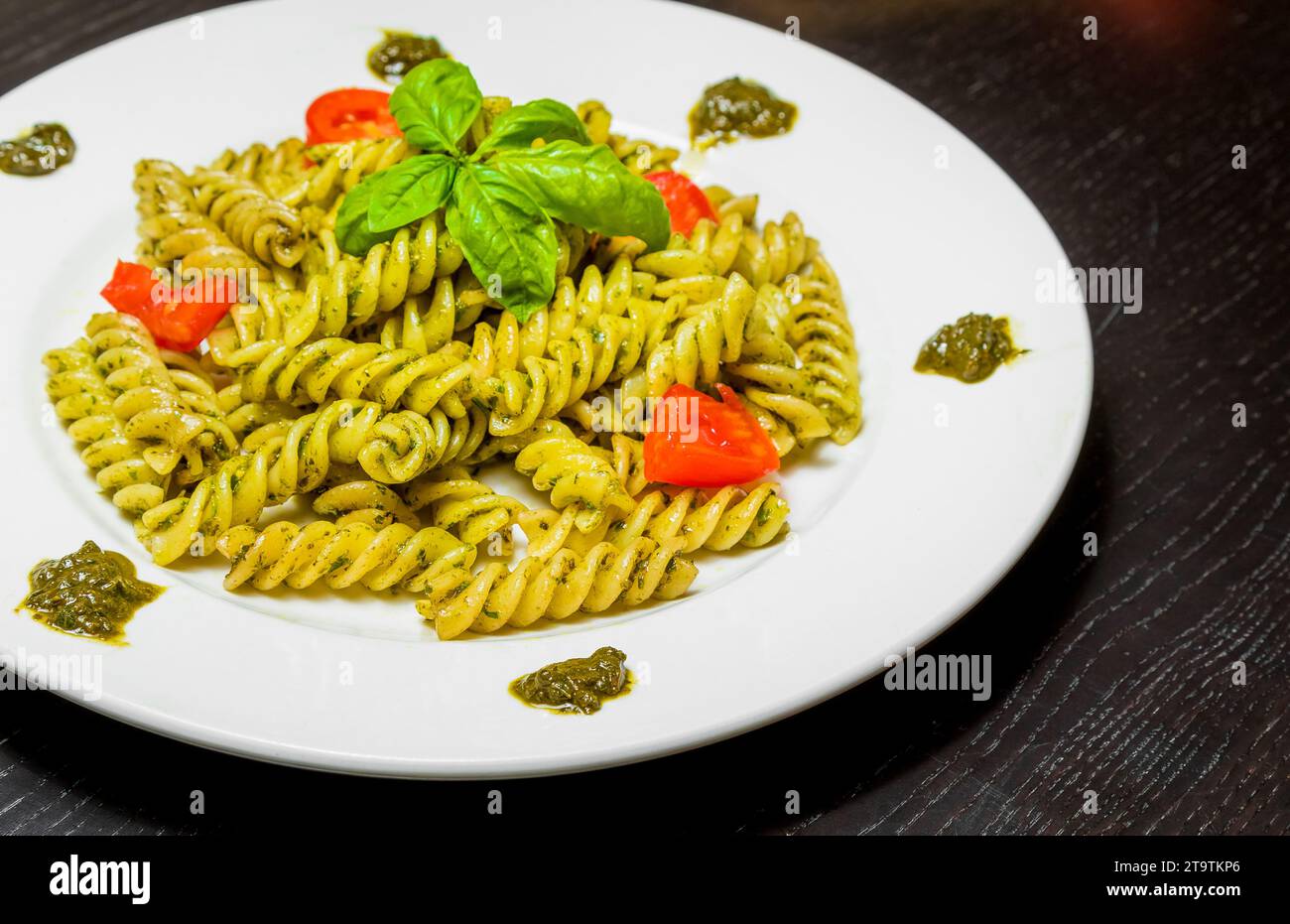 Gericht mit Pasta mit Pesto-Genovese-Sauce und Gemüse, Tomaten und Basilikum auf schwarzem Holztisch Stockfoto