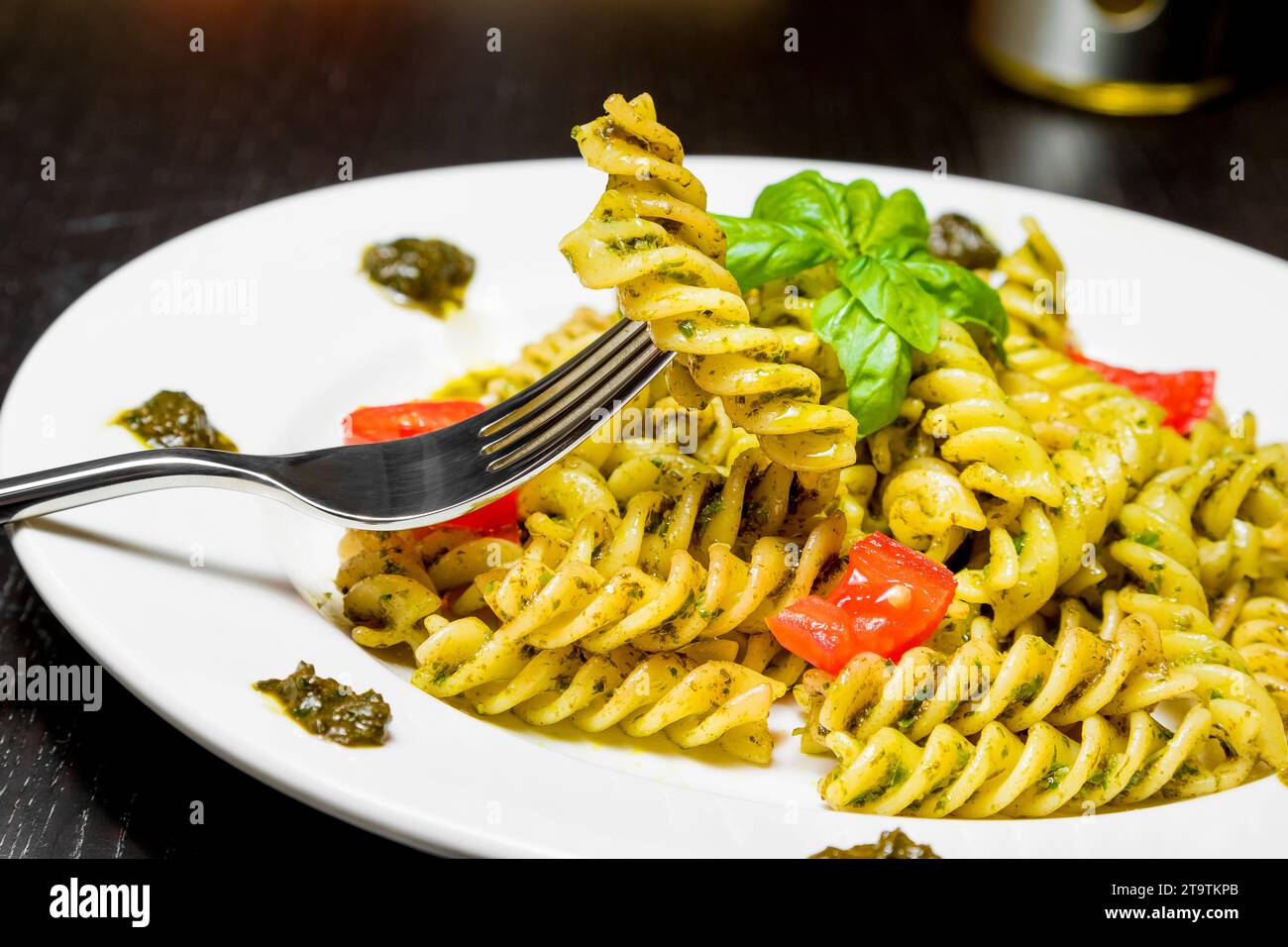 Gericht mit Pasta mit Pesto-Genovese-Sauce und Gemüse, Tomaten und Basilikum, Detail der Gabel mit Fusilli auf schwarzem Holztisch Stockfoto