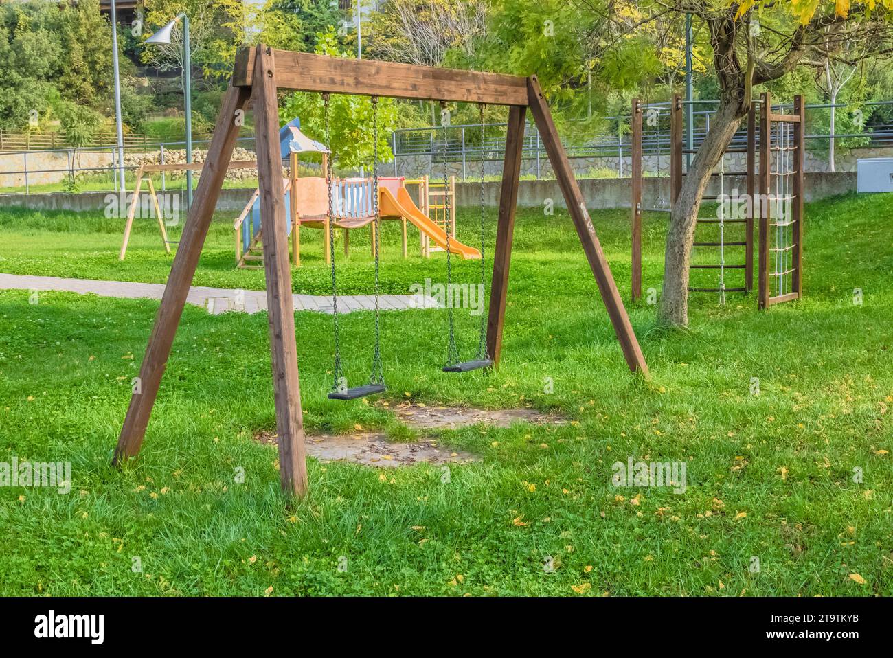 Leere Schaukeln auf dem Spielplatz für Kinder in der Nähe von Treppen Rutschen Ausrüstung, auf grüner Wiese Hintergrund Stockfoto