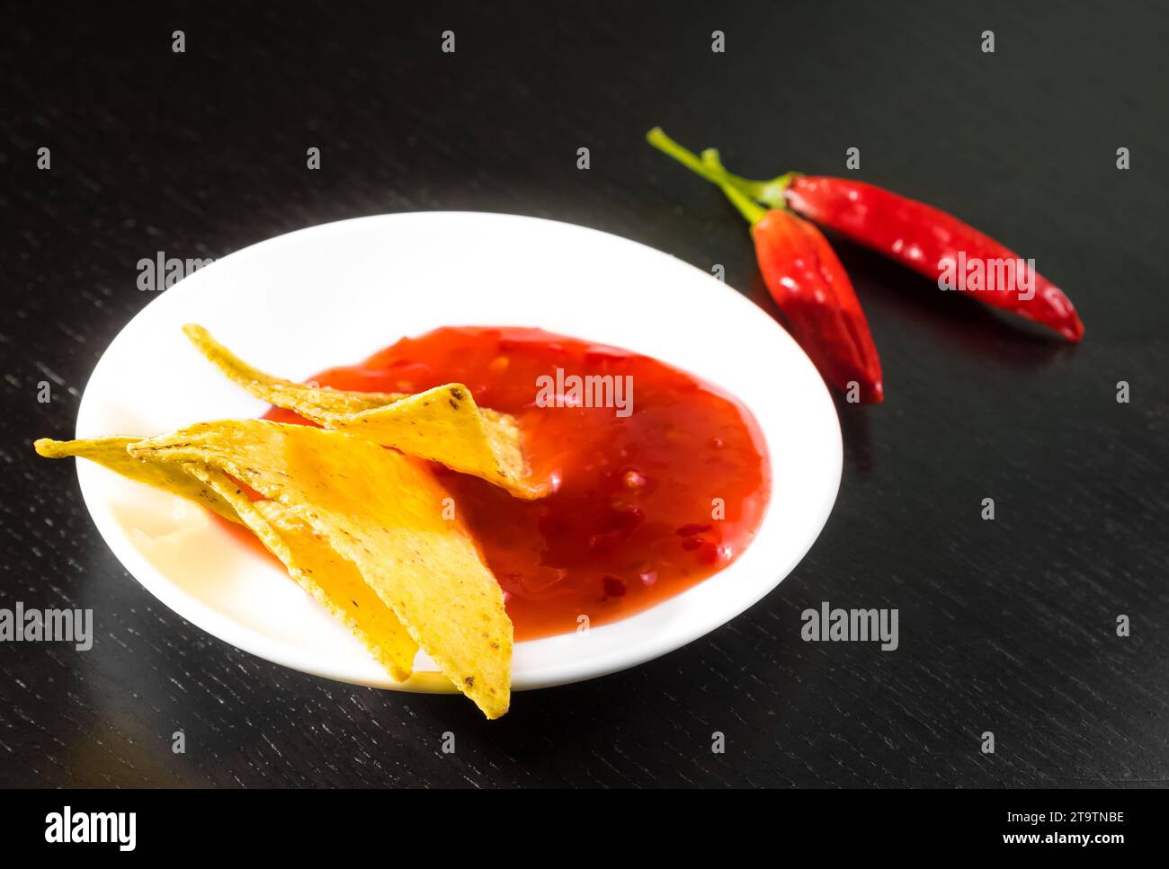 Knusprige Maisnachos mit scharfer Tomatensauce als Snack oder Vorspeise in einer weißen Scheibe auf schwarzem Holztisch Stockfoto