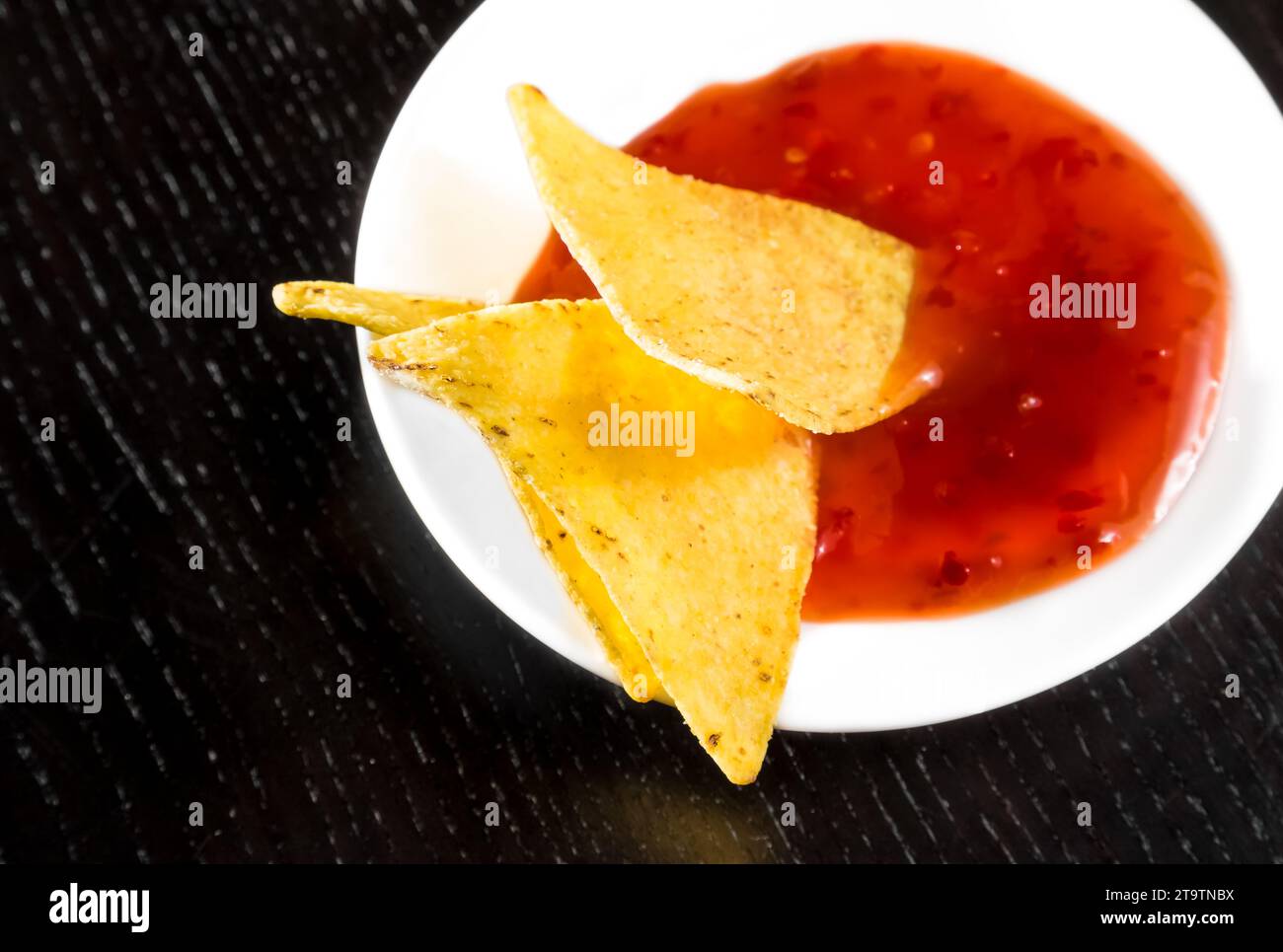 Knusprige Maisnachos mit scharfer Tomatensauce als Snack oder Vorspeise in einer weißen Scheibe auf schwarzem Holztisch Stockfoto