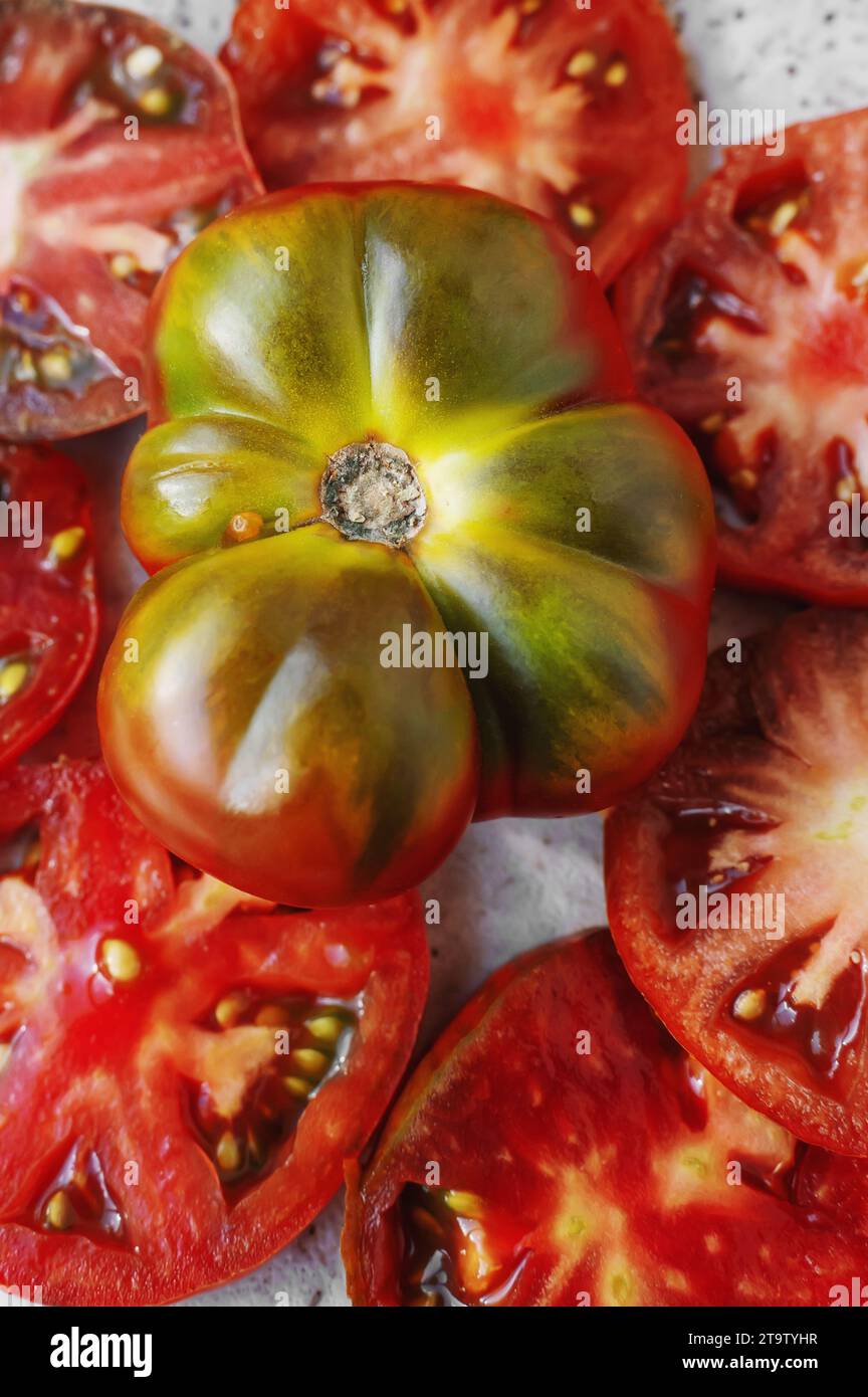 Hintergrund zerlegter Sortentomaten. In der Mitte ist eine ganze Tomate in rot-grüner Farbe. Nahaufnahme Stockfoto