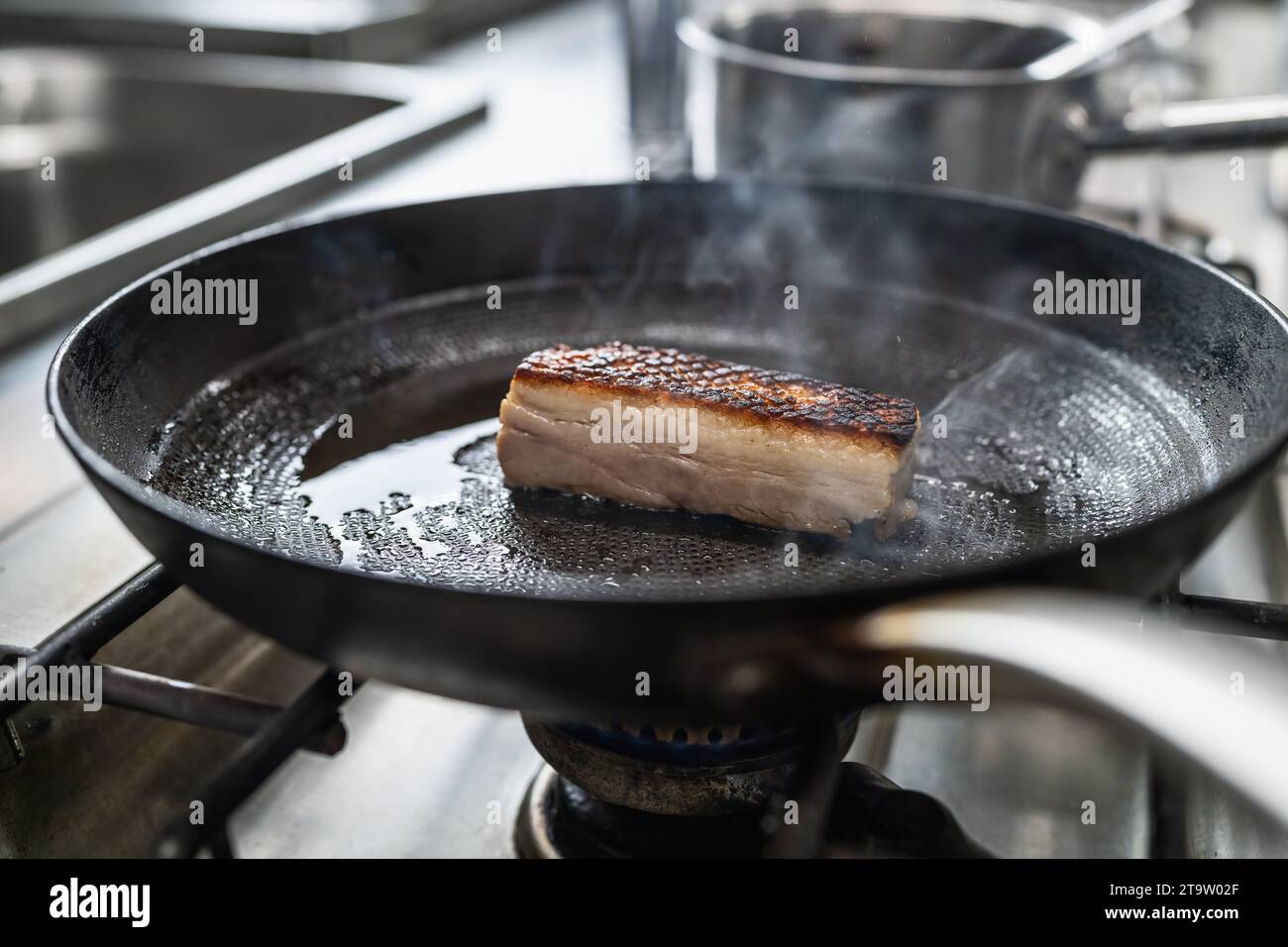 Knusprige Schweinebauchbraten in einer heißen Pfanne mit Öl an einem Gasherd in einer professionellen Küche in einem Restaurant. Bild des Kochkonzepts des Luxushotels. Stockfoto