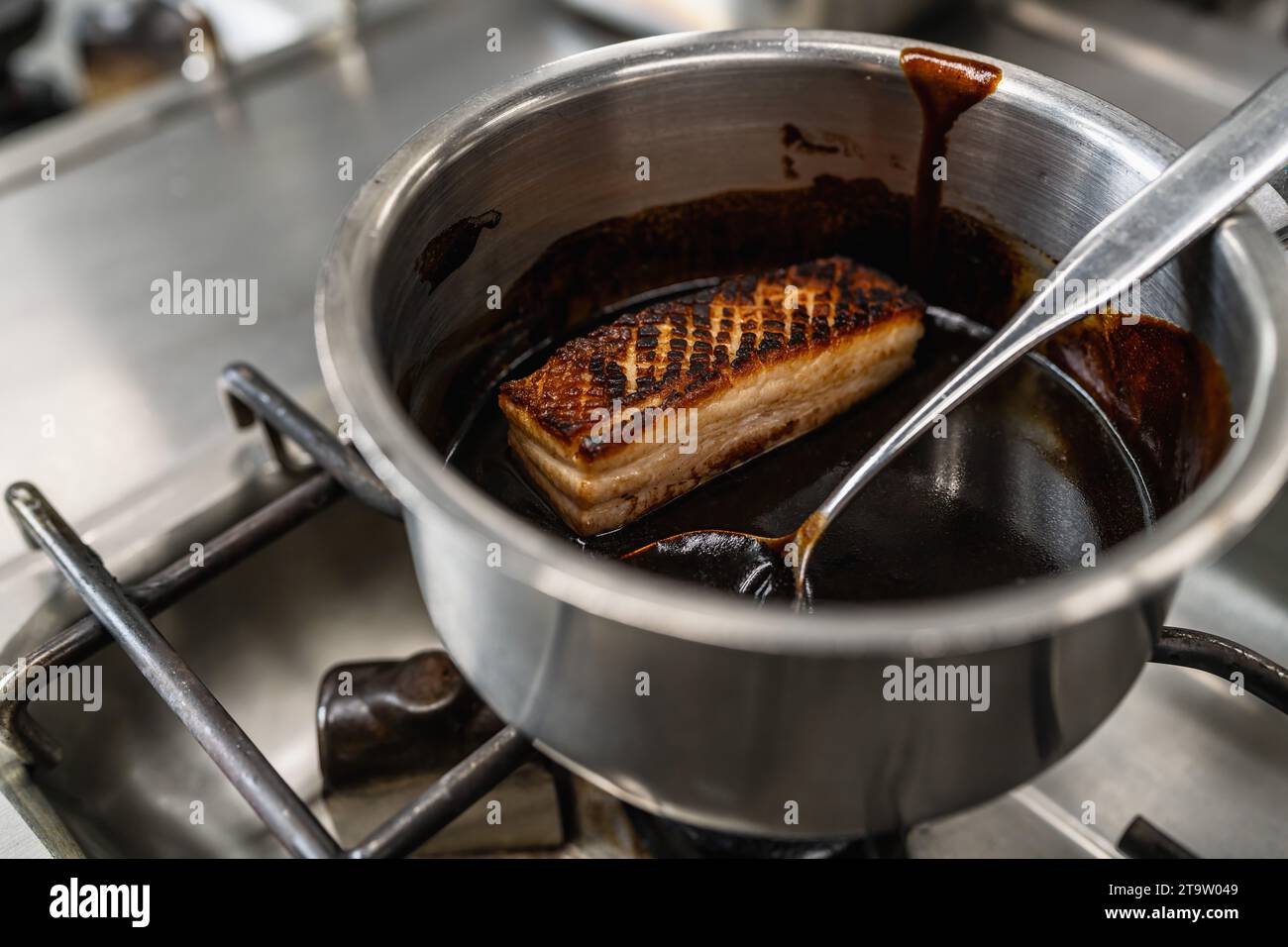 Knusprig gebratenes Schweinefleisch glasiert mit brauner Sauce in einem Topf in einer professionellen Küche in einem Restaurant. Bild des Kochkonzepts des Luxushotels. Stockfoto