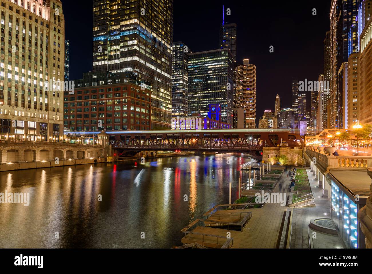 Nächtlicher Blick auf die Innenstadt von Chicago und den Fluss. Leichte Spuren, die von einem vorbeifahrenden Zug hinterlassen werden, sind auf der Brücke im Vordergrund zu sehen. Stockfoto