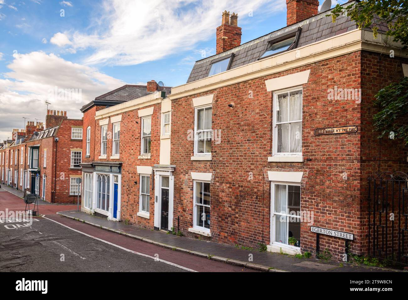 Reihe alter britischer Terrassenhäuser entlang einer Straße unter blauem Himmel mit Wolken bei Sonnenuntergang Stockfoto
