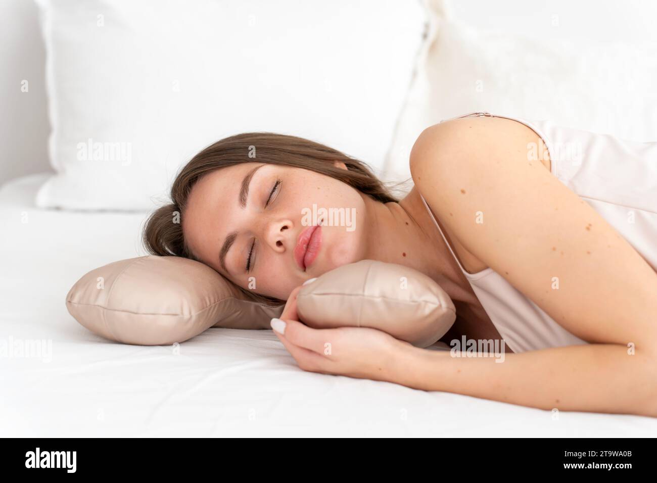 Weißes sexy Mädchen 20-25 Jahre alt in Seidenwäsche schläft auf einem Schönheitskissen auf einem weißen Bett im Schlafzimmer. Gesunder Schlaf auf einem komfortablen Bett. Drehen Stockfoto