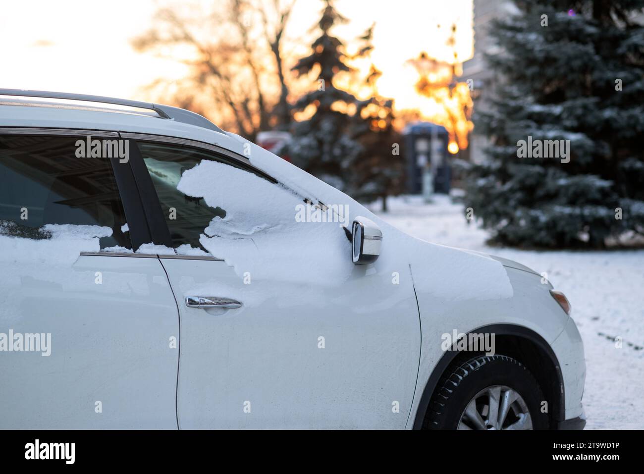 Seitenansicht eines weißen Autos mit gefrorenen Seitenscheiben. Ein Auto, das bei Sonnenuntergang in der Winternähe mit einer Schneeschicht bedeckt ist Stockfoto