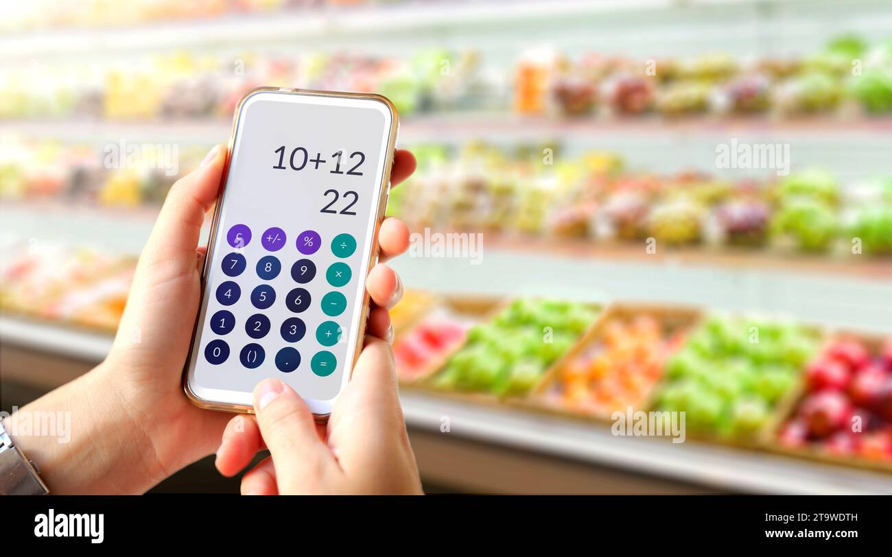 Taschenrechner auf dem Bildschirm des Mobiltelefons in den Händen des Kunden. Die junge Frau schreibt im Supermarkt mit einem Taschenrechner. Stockfoto