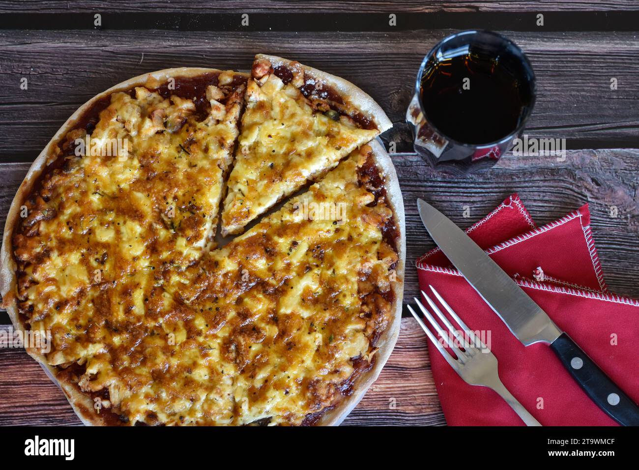 Frisch gebackene hausgemachte Pizza auf rustikalem Holztisch. Hühnchenpizza mit Käse, Pizzascheibe. Rote Serviette, Messer und Gabel, Glas Limonade. Draufsicht. Stockfoto