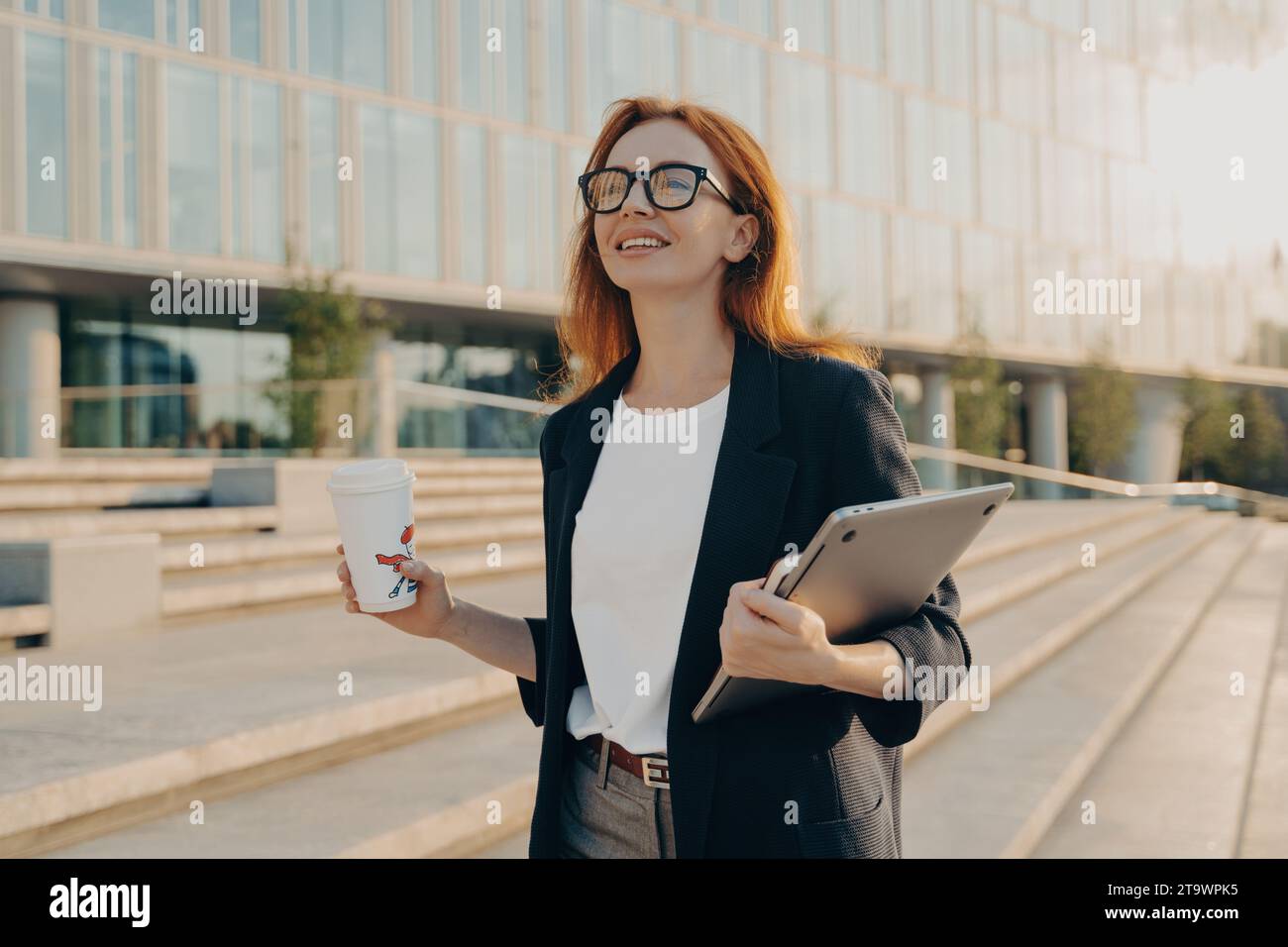 Optimistische Geschäftsfrau mit Kaffee und Tablet, die an einem Büro vorbeiläuft und bereit für den nächsten Tag ist Stockfoto