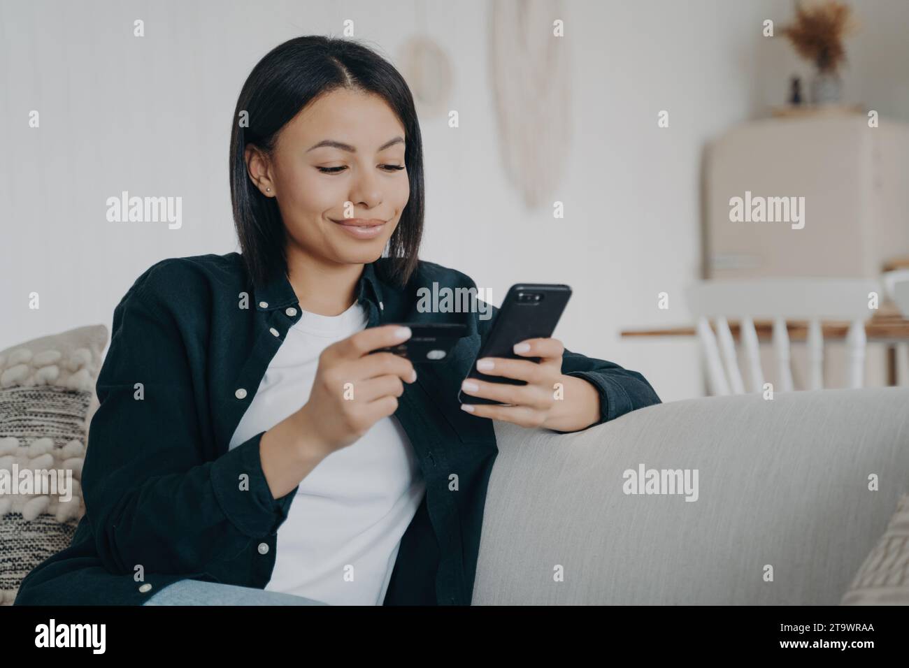 Lächelnde junge Frau, die ihr Smartphone für Online-Banking zu Hause nutzt Stockfoto