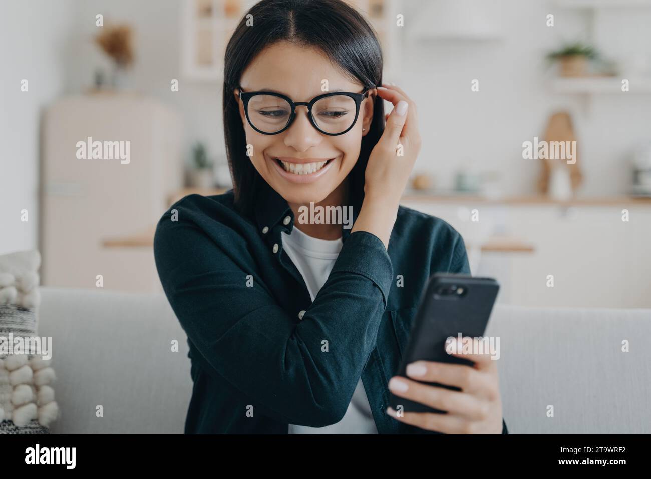 Fröhliche junge Frau, die zu Hause auf ihrem Smartphone eine Unterhaltung genießt Stockfoto