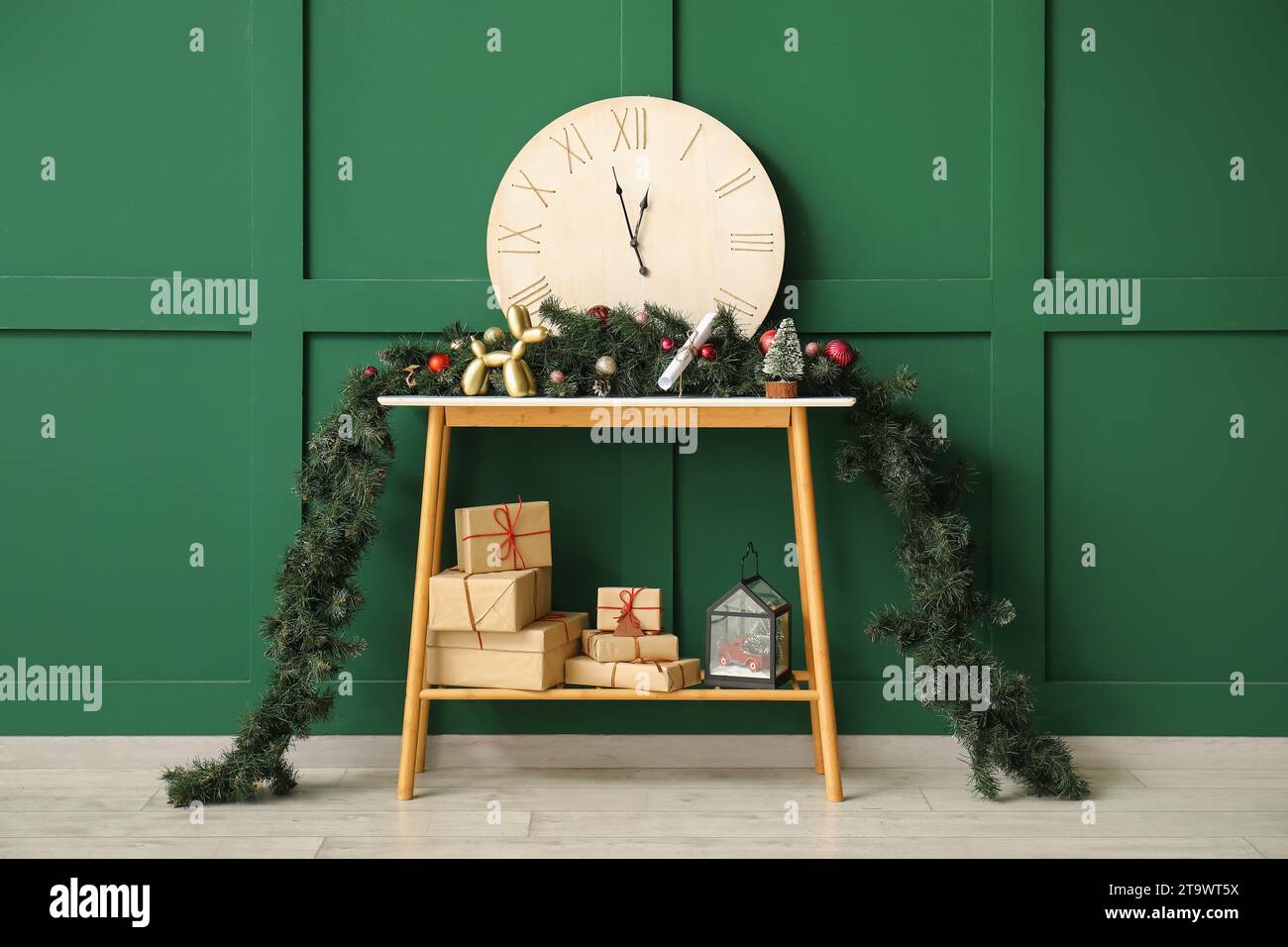 Konsolentisch mit Geschenkboxen, Uhr, Tannenzweigen und weihnachtlicher Einrichtung an der grünen Wand Stockfoto