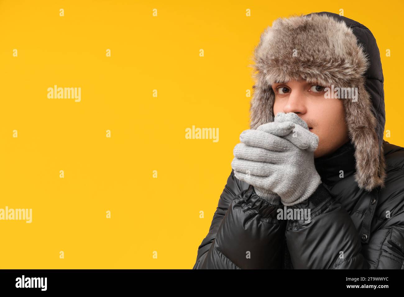 Junger Mann in schwarzer stilvoller Pufferjacke und Hut auf gelbem Hintergrund Stockfoto