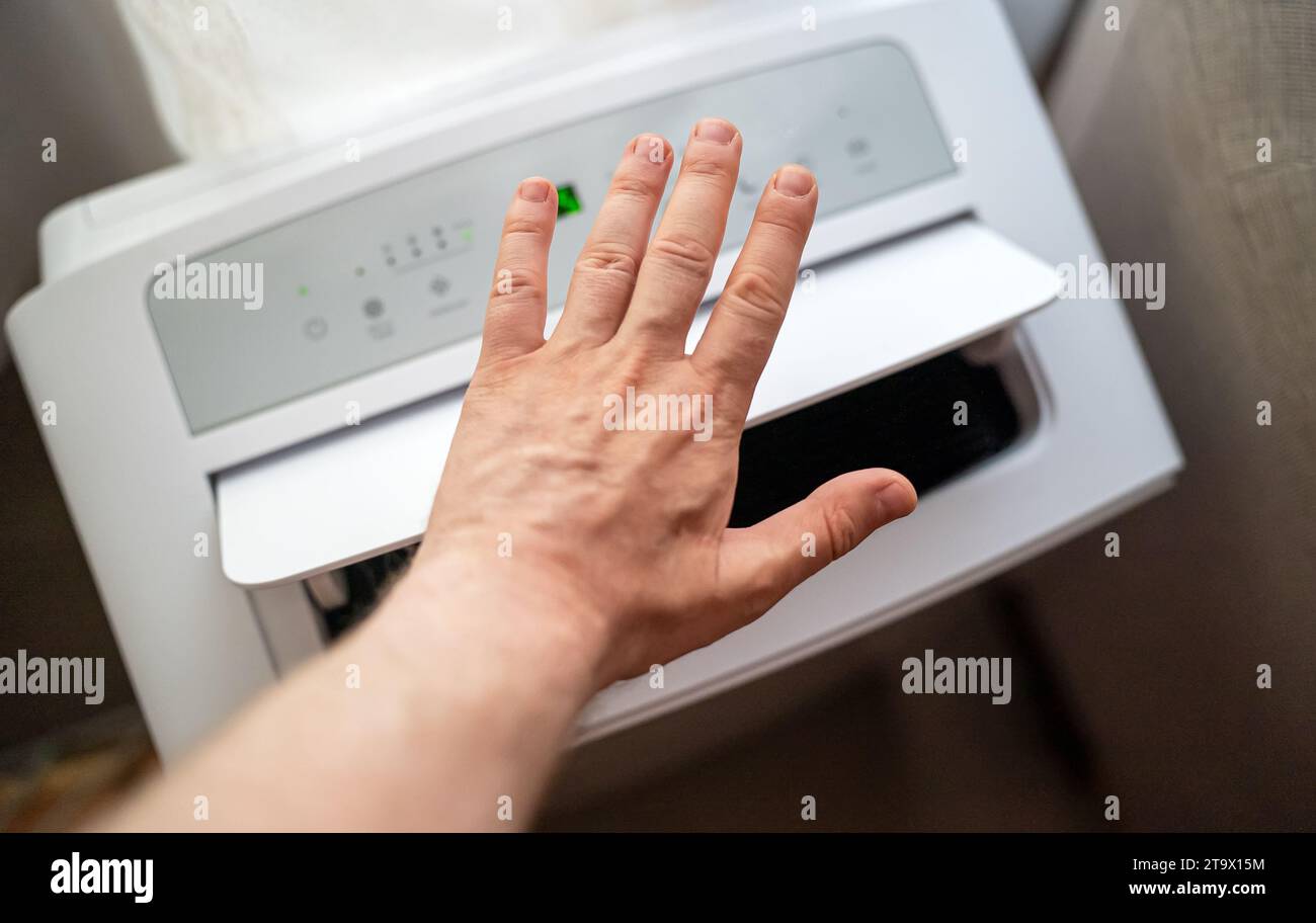 Männliche Hand, die den Luftstrom der mobilen Klimaanlage im Boden überprüft. Stockfoto