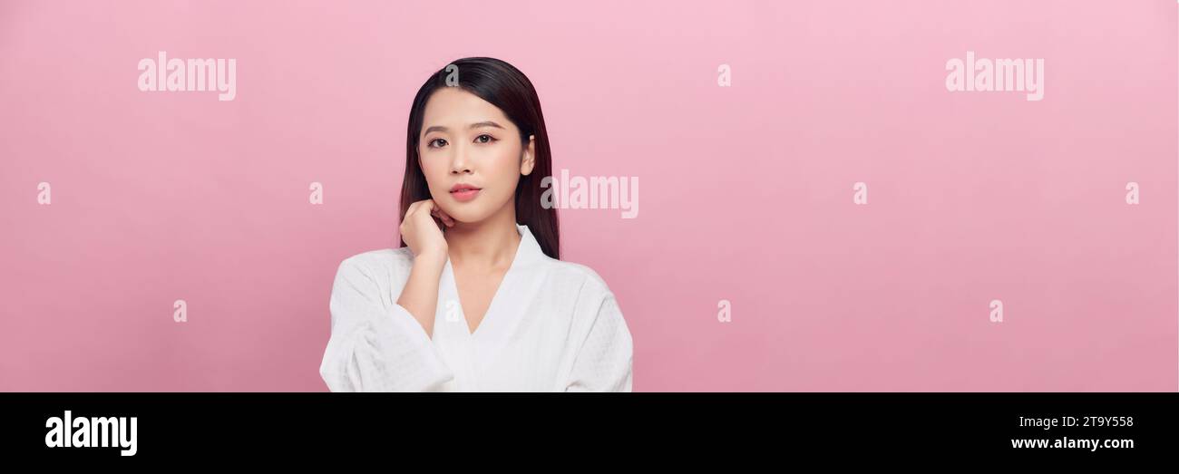 Schönes asiatisches Mädchen-Modell mit natürlichem Make-up, das glühende, hydrierte Haut auf rosa Hintergrund berührt, Panorama Stockfoto
