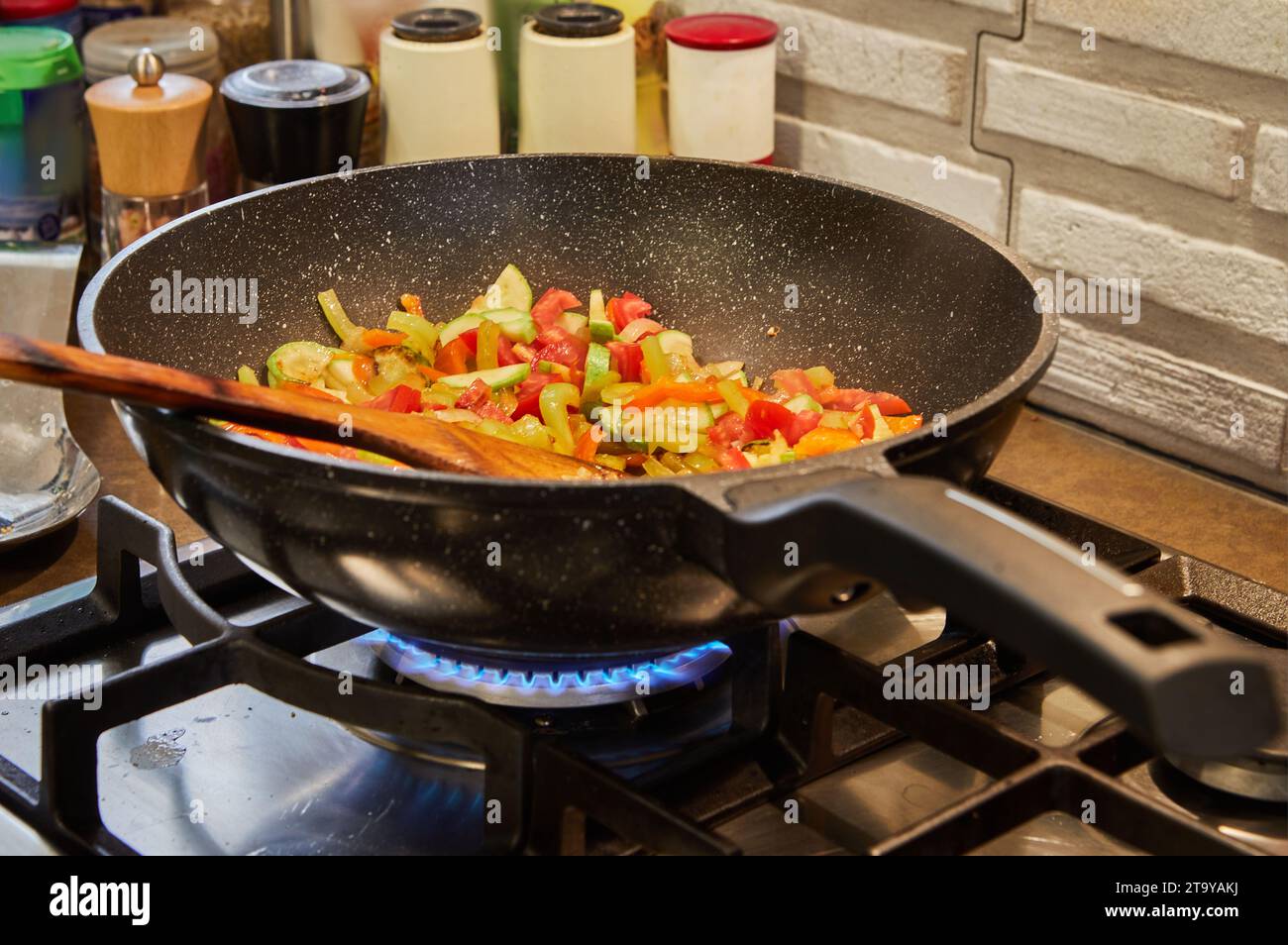 Die Pfanne mit Schüssel und Holzstab zum Rühren wird auf dem Feuer des Gasherds gekocht. Stockfoto