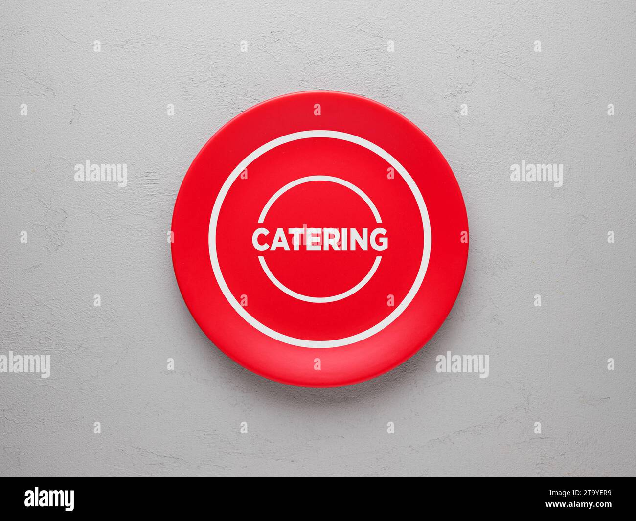 Das Wort Catering auf einer roten Keramikplatte über strukturiertem grauen Hintergrund. Draufsicht. Stockfoto