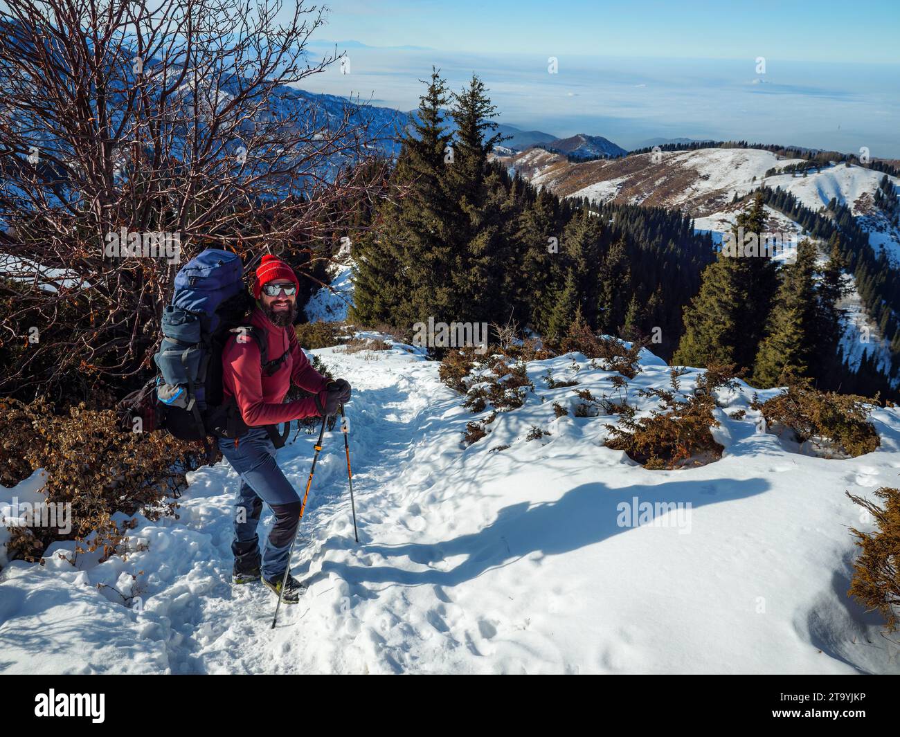 Bärtiger Mann mit Rucksack wandert im Winter in die Berge. Schönes Wetter an einem sonnigen Wintertag draußen in den Bergen Stockfoto