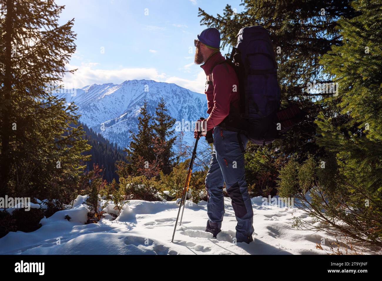 Ein männlicher Tourist wandert in den Bergen. Bärtiger Reisender mit großem Rucksack. Schönes Wetter an einem sonnigen Wintertag draußen in den Bergen Stockfoto