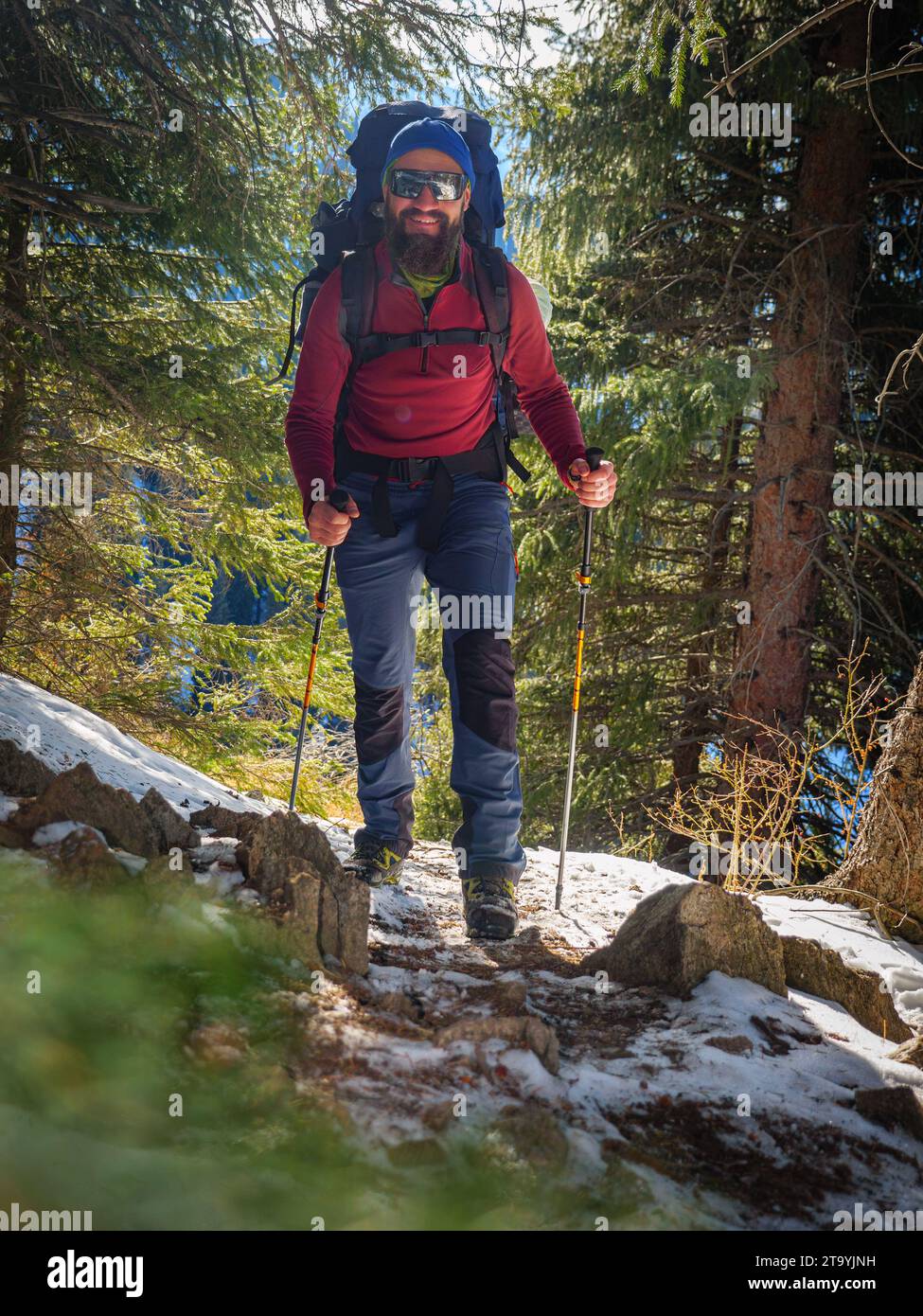 Bärtiger Mann mit Rucksack wandert im Winter in die Berge. Schönes Wetter an einem sonnigen Wintertag draußen in den Bergen Stockfoto