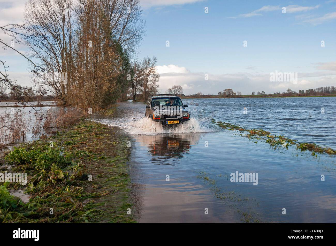 Ein Auto, das aufgrund von starkem Regen und Windfaktor durch eine überflutete Straße gefahren wird. Das nationale Koordinierungskomitee für Hochwassergefahr (LCO) des Rijkswaterstaates trat am Donnerstag aufgrund der erwarteten hohen Wasserstände an der Küste, am IJsselmeer und an den großen Flüssen in Aktion. Eine solche Situation ist laut Rijkswaterstaat selten. Die Sturmflut-Barrieren Hollandse IJsselkering in Zuid-Holland und die Haringvlietsluizen werden am Donnerstagabend geschlossen. Das Ramspolkering in der IJssel bei Kampen wird wahrscheinlich später geschlossen. Das Wasser entlang der Küste wird von starken Winden hochgetrieben. Das KNM Stockfoto