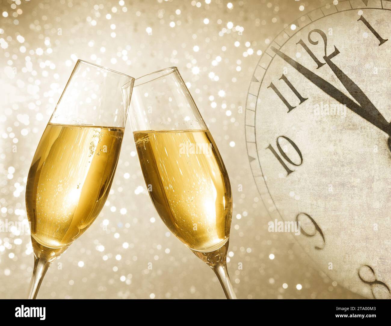 Champagnerflöten mit goldenen Blasen lassen auf silbernem Bokeh-Hintergrund mit Vintage-Wecker jubeln, der Mittag- oder Mitternacht zeigt, Happy New Year-Konzept Stockfoto