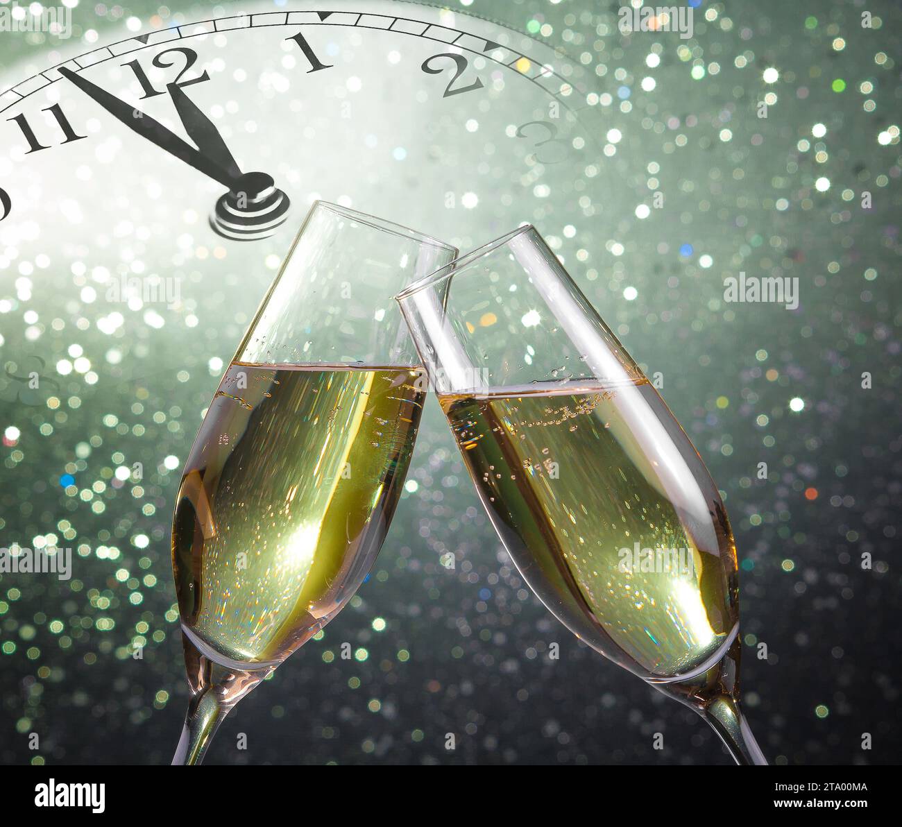 Champagnerflöten mit goldenen Blasen lassen auf grünem Bokeh-Hintergrund mit Vintage-Wecker jubeln, der Mitternacht zeigt, Happy New Year-Konzept Stockfoto