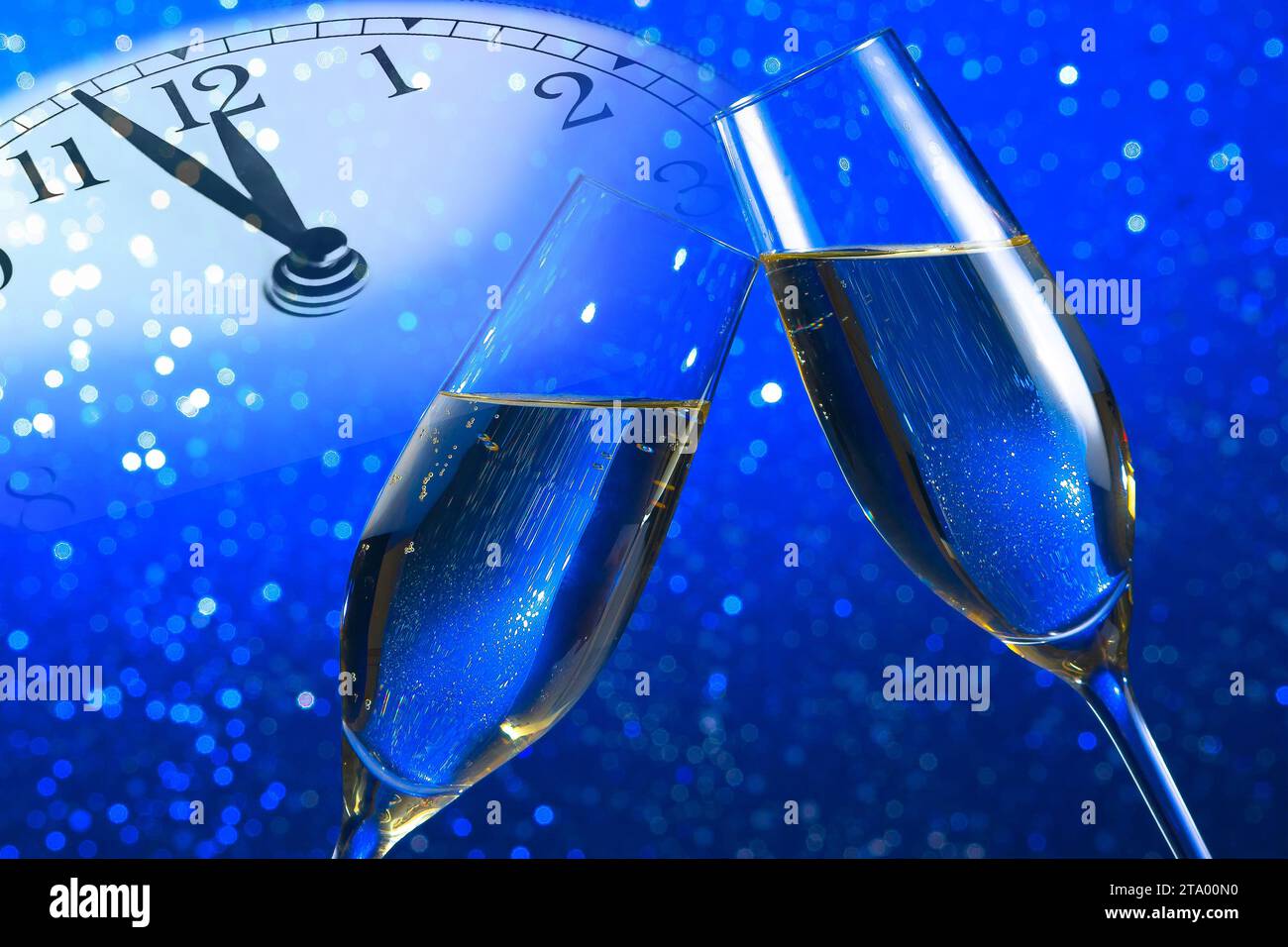 Champagnerflöten mit goldenen Blasen lassen auf blauem Bokeh-Hintergrund mit Vintage-Wecker jubeln, der mittags oder mitternacht ein Happy New Year-Konzept zeigt Stockfoto
