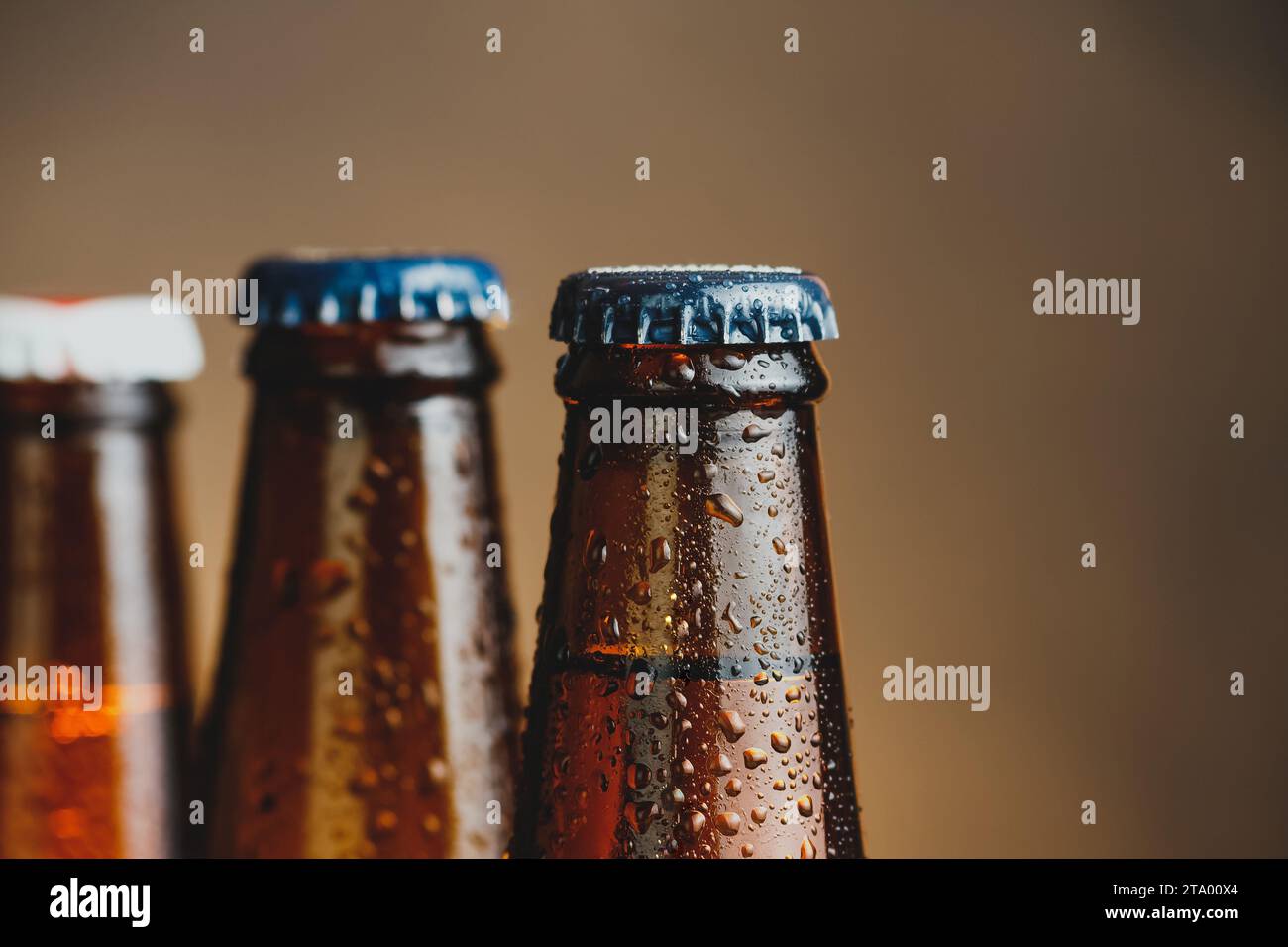 Nahaufnahme von frischen, kalten Bierflaschen mit Tropfen und Fokus auf den Stopfen auf warmem Hintergrund Stockfoto