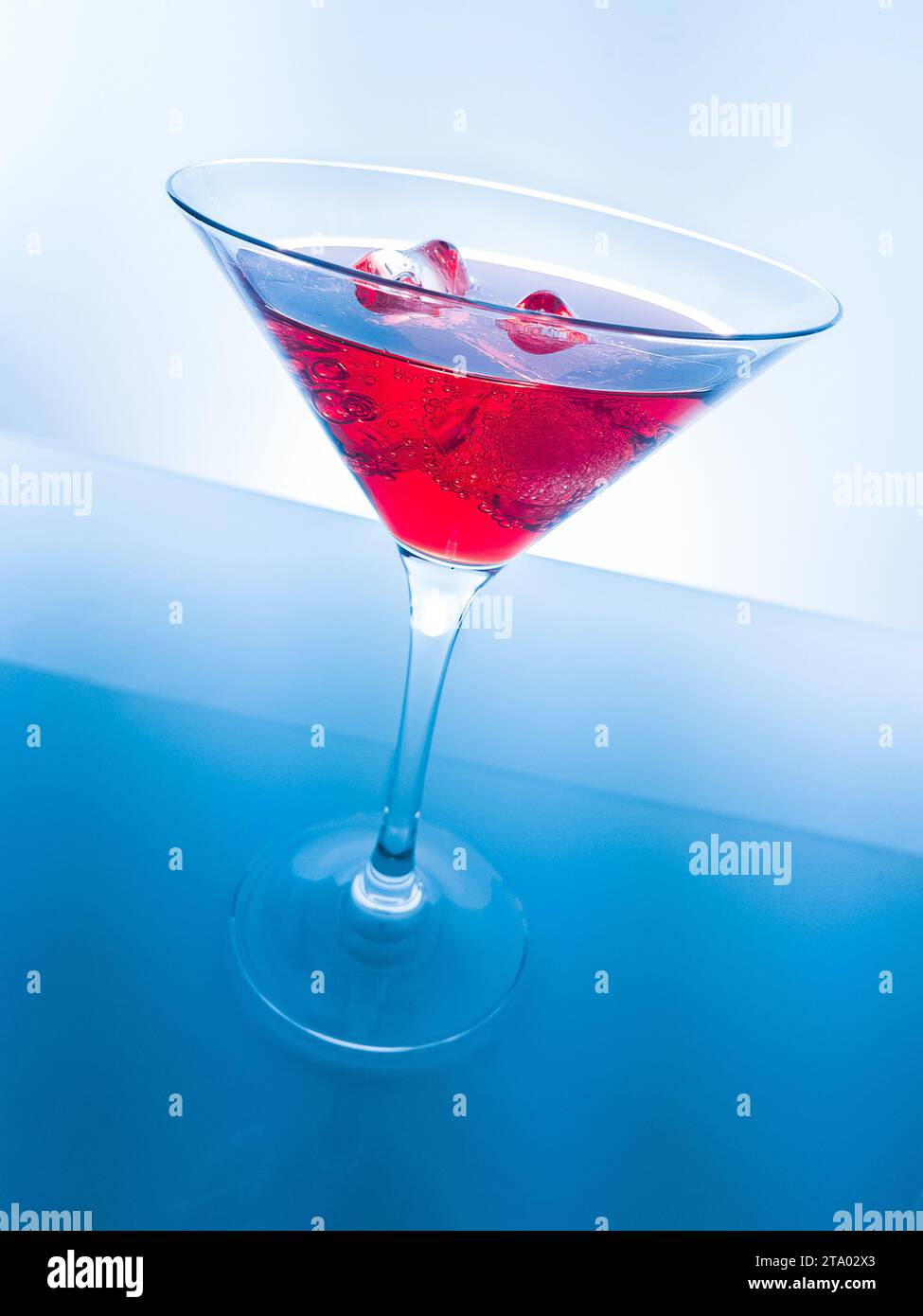 Rotes Cocktail-Getränk mit Eiswürfeln auf blauem Hintergrund, lustiges und tanzendes Disco-Konzept Stockfoto