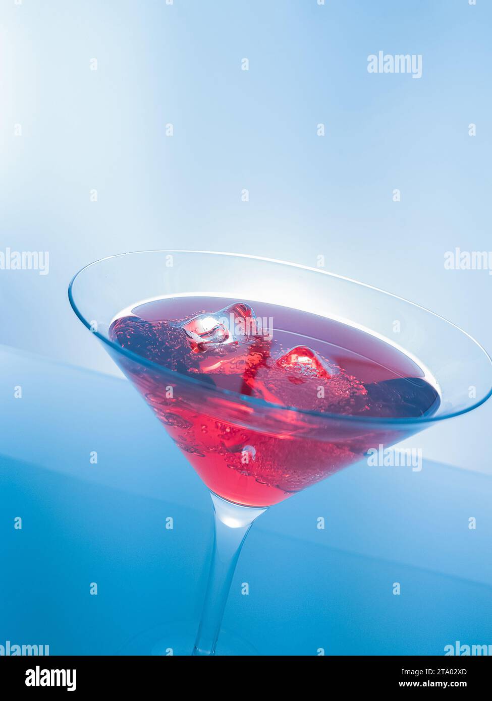 Rotes Cocktail-Getränk mit Eiswürfeln auf blauem Hintergrund, lustiges und tanzendes Disco-Konzept Stockfoto