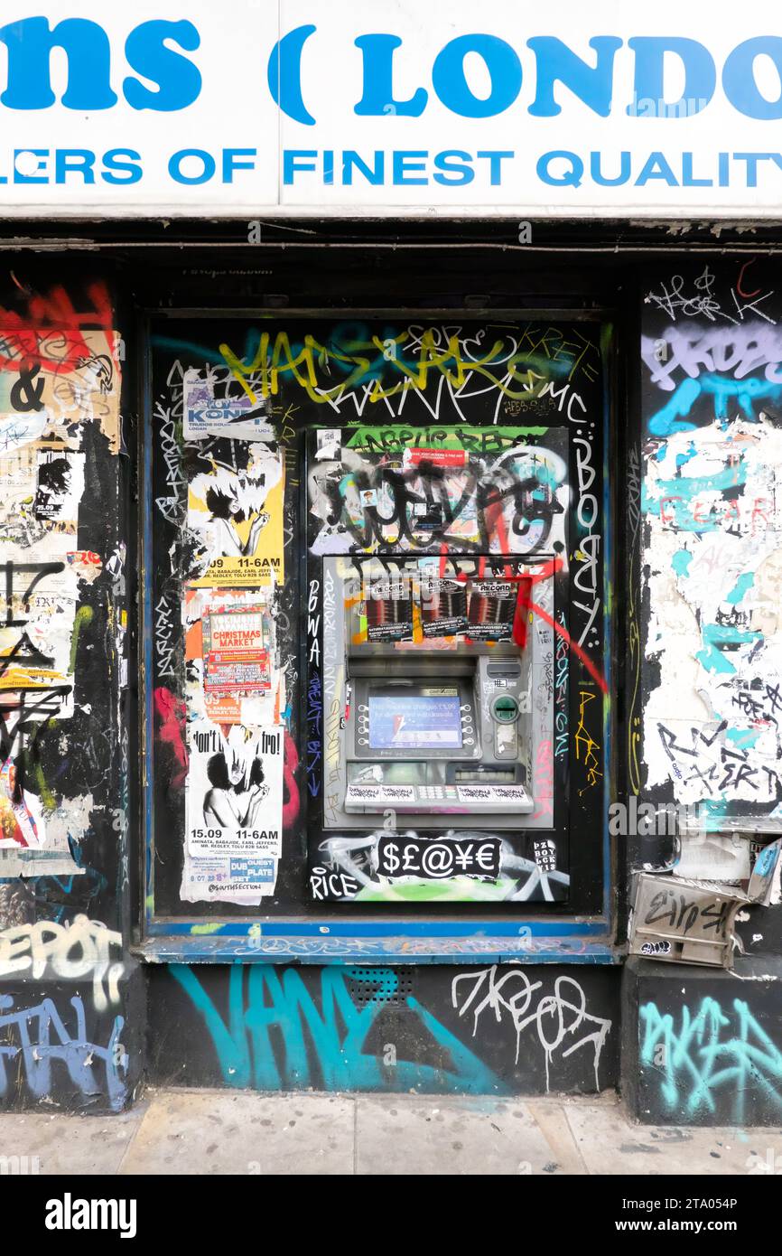 Ein Geldautomat oder Geldautomat, der in die Wand eines Gebäudes eingebaut ist. Der Geldautomat befindet sich an der Straße. Es ist in Betrieb, ist aber komplett mit Graffiti und Aufklebern bedeckt Stockfoto