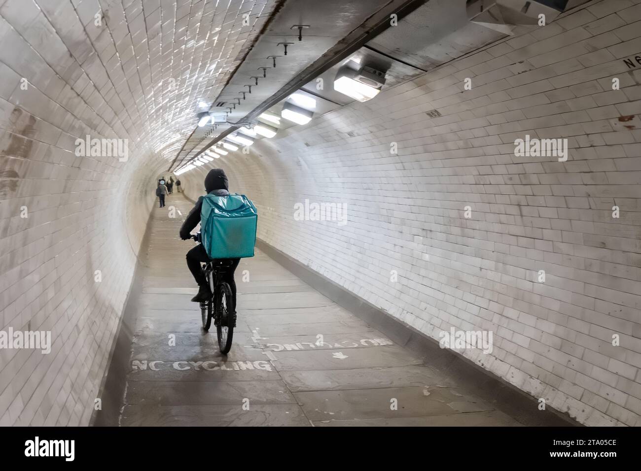 Ein Deliveroo-Radfahrer, der mit dem Fahrrad durch den Greenwich Foot Tunnel fährt. Der Tunnel verläuft unter der Themse und verbindet die Isle of Dogs mit Greenwich Stockfoto