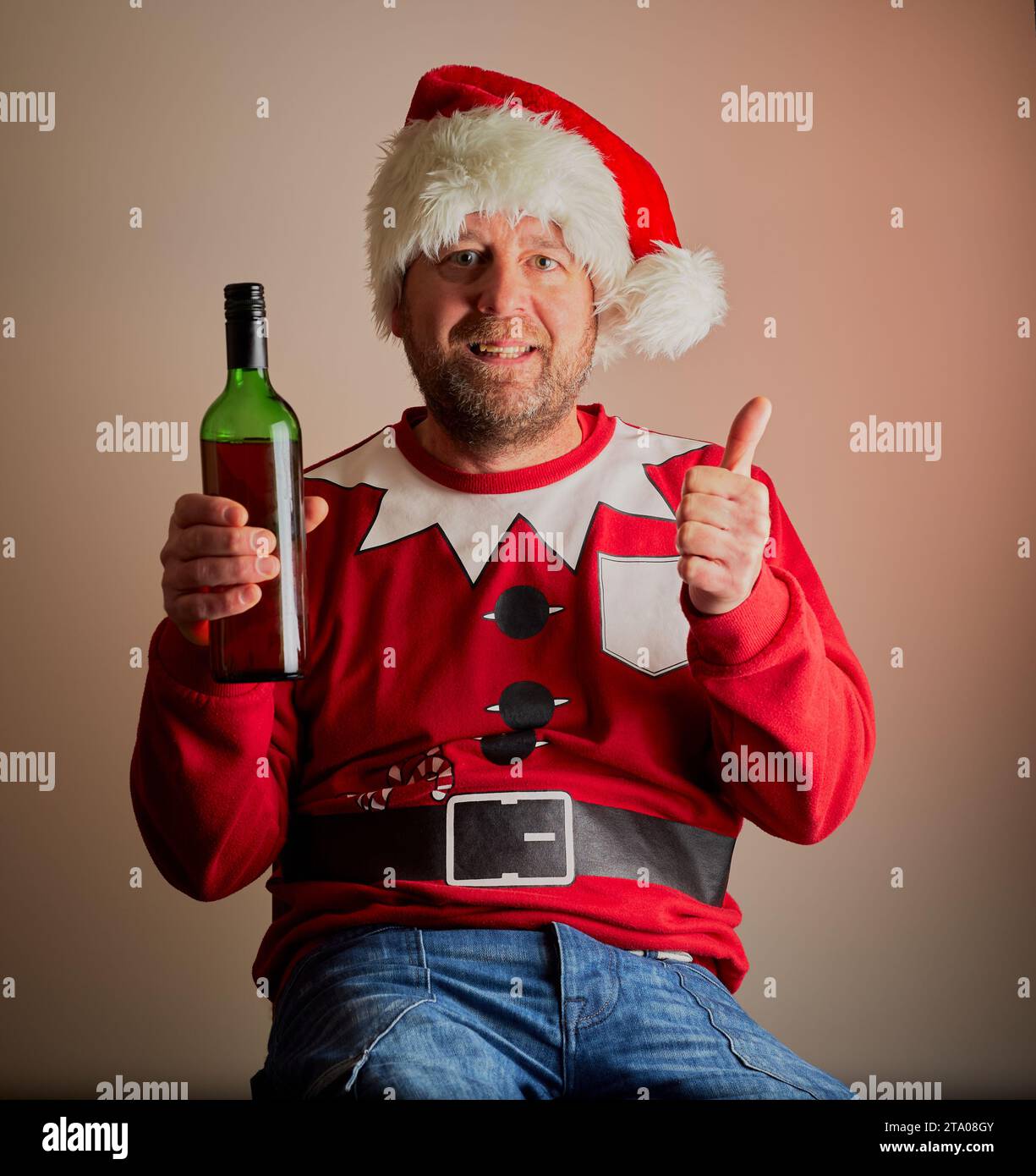 Ein Mann, der als Weihnachtsmann gekleidet ist und eine Flasche Wein mit einem schönen Hintergrund hält. Stockfoto