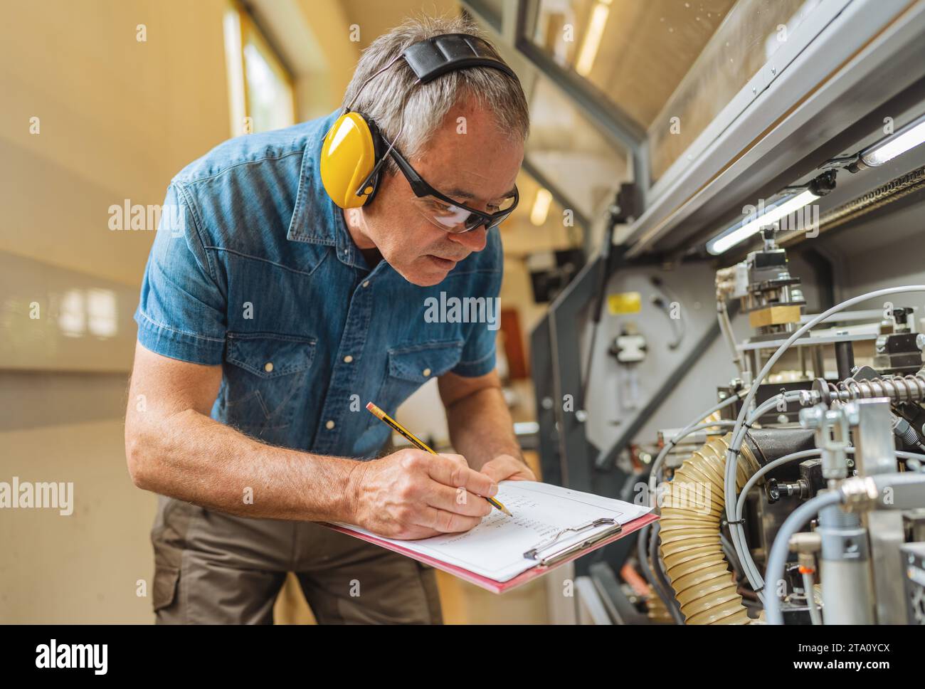 Techniker mit Gehörschutzbeschriftung auf Klemmbrett im industriellen Umfeld Stockfoto