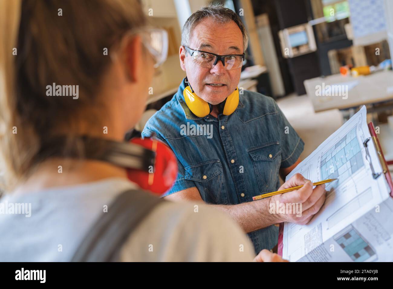 Tischlerlehrer diskutiert mit einem Auszubildenden in einer Tischlerwerkstatt Baupläne Stockfoto