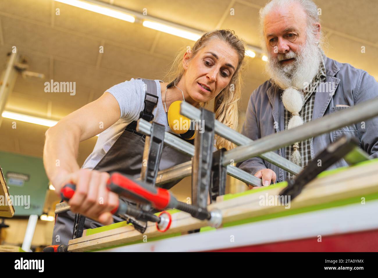 Schreinermeister und Lehrling mit einer Klammer für Holzverleimung in einer Werkstatt Stockfoto