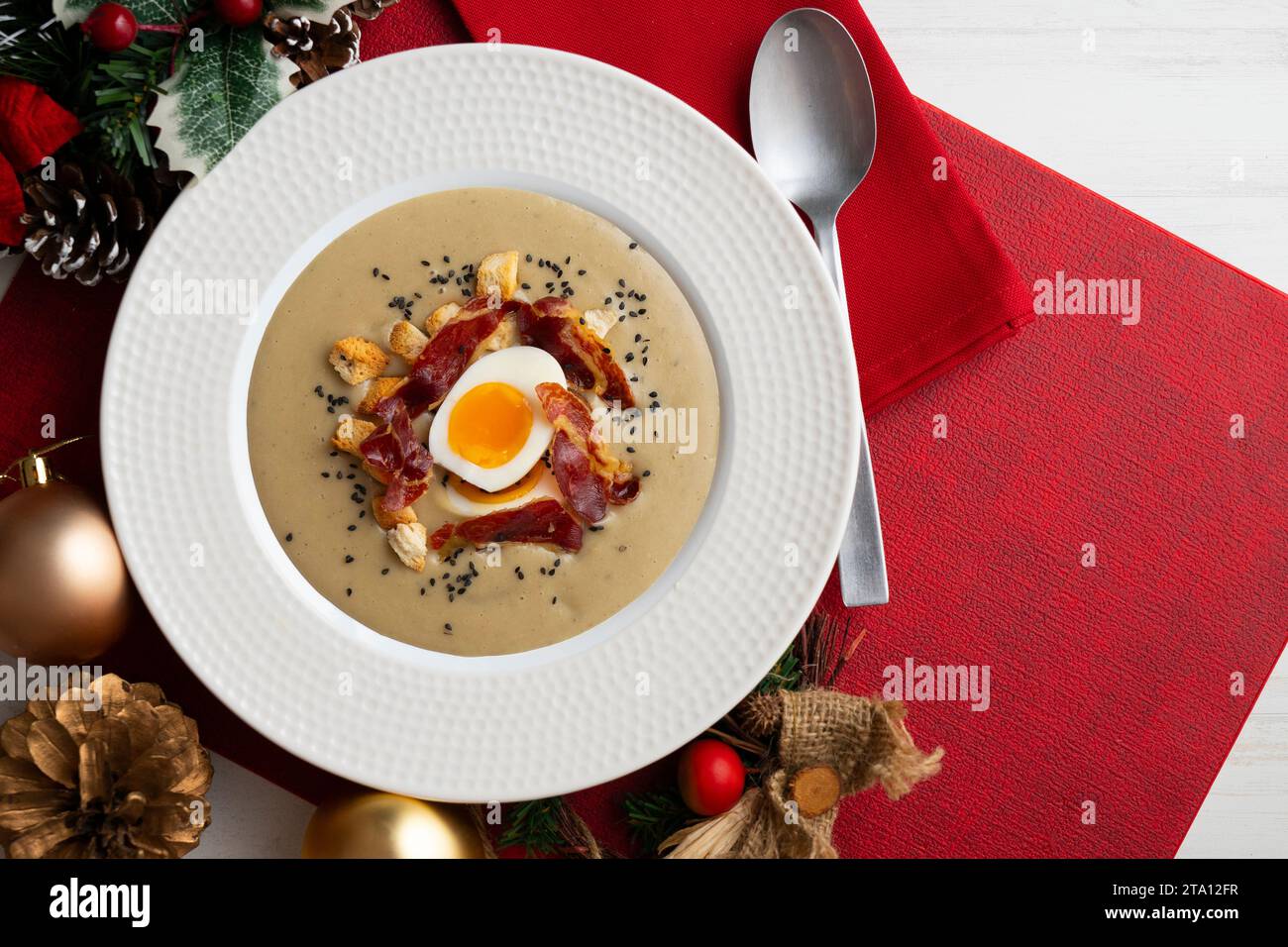 Geräucherte Auberginencreme mit knusprigem iberischem Schinken und gekochtem Ei. Weihnachtsessen auf einem Tisch mit Weihnachtsmotiven. Stockfoto